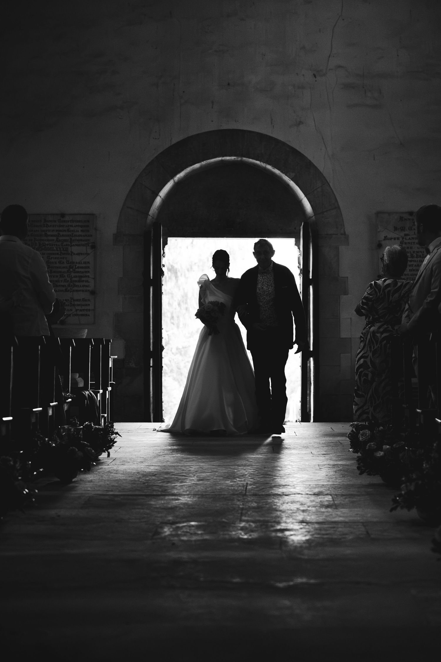 Black and white silhouette of bride and groom entering church through arched doorway on wedding day.