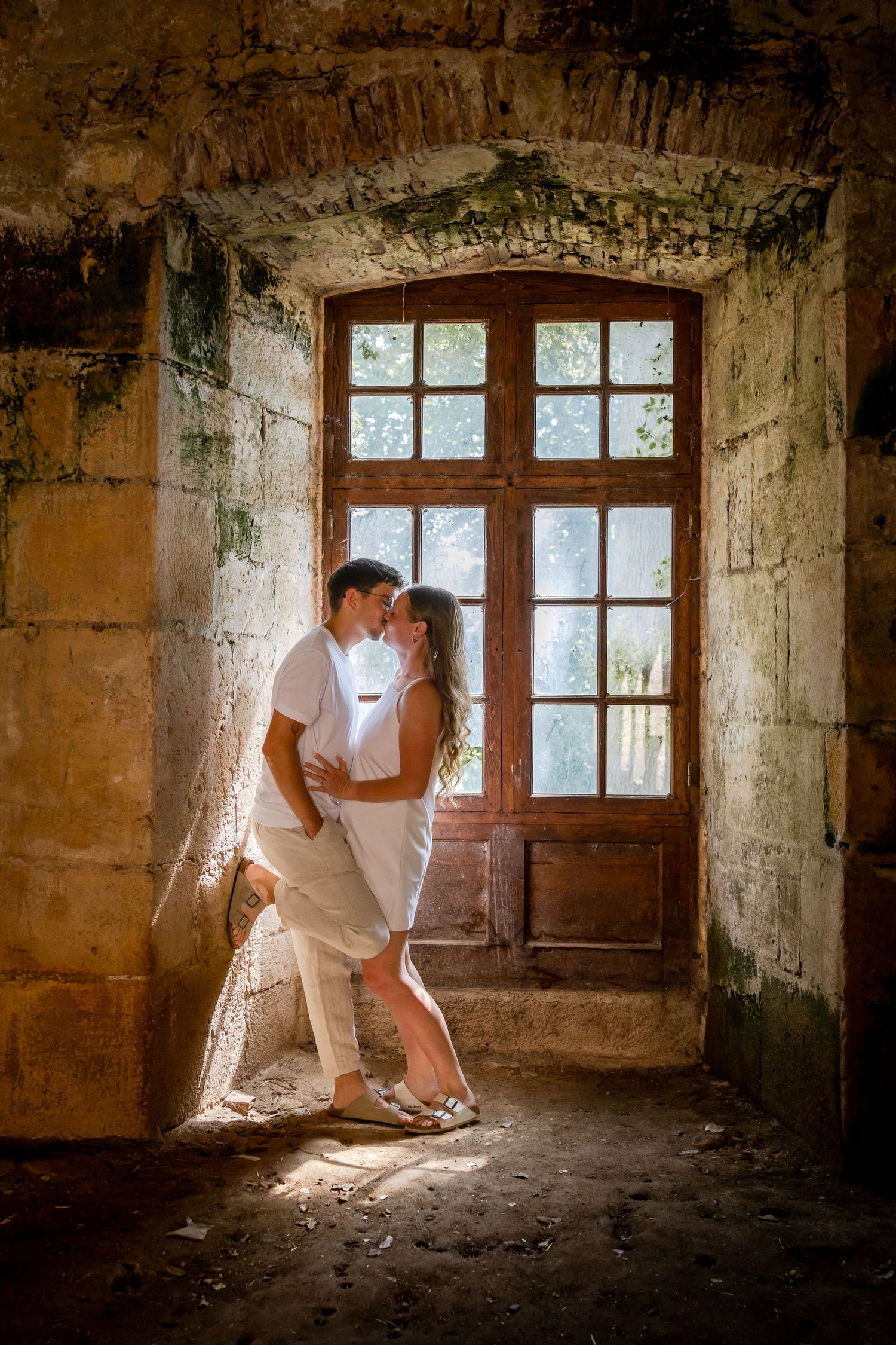 Couple in white embracing near rustic wooden door in ancient stone building, romantic photography.