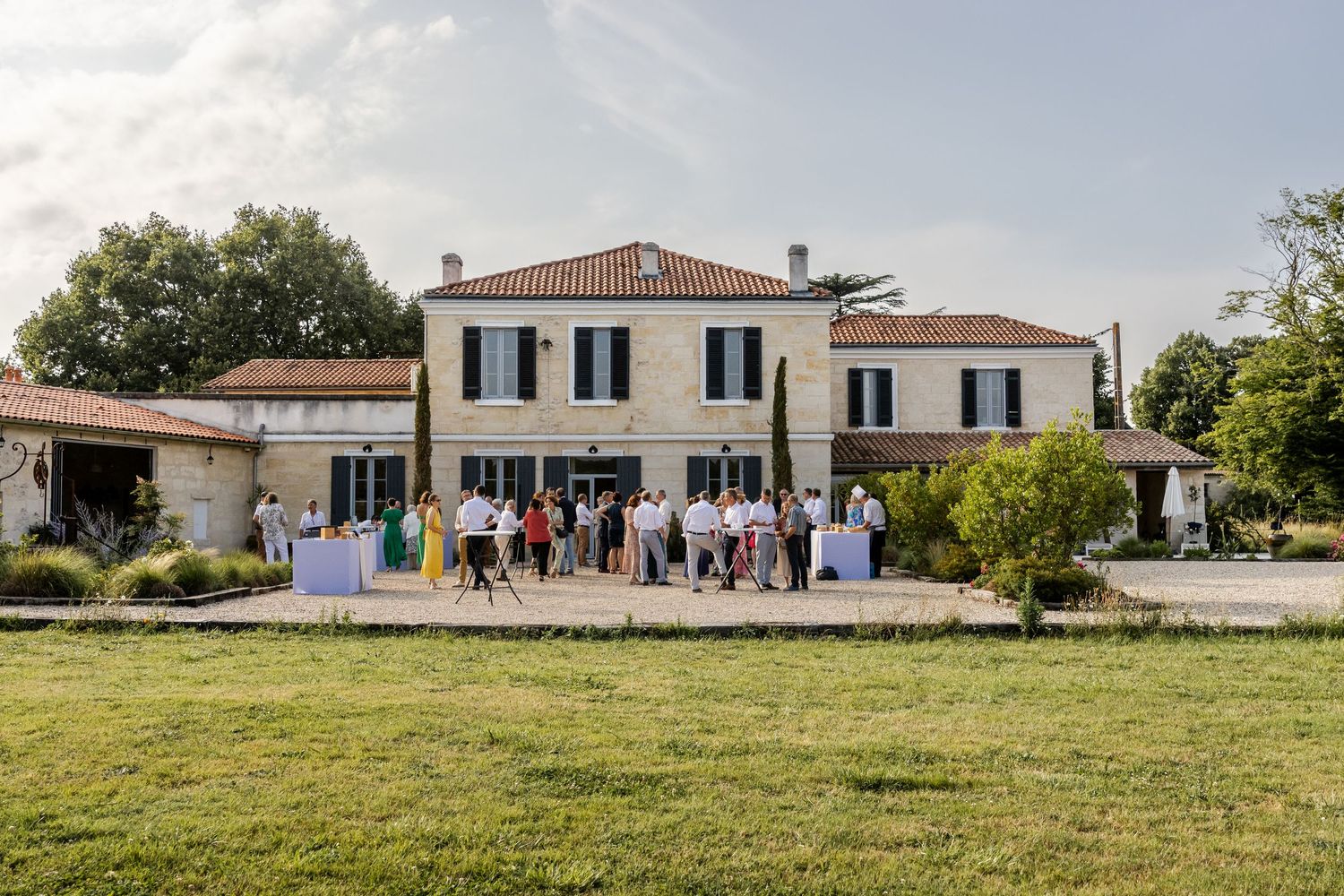 Elegant French country estate with guests gathered outside for an outdoor event on a sunny day.