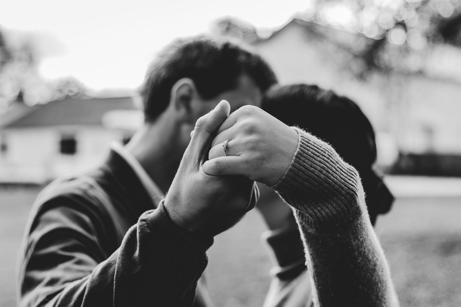 Black and white photo of a couple holding hands and kissing outdoors near a white building.