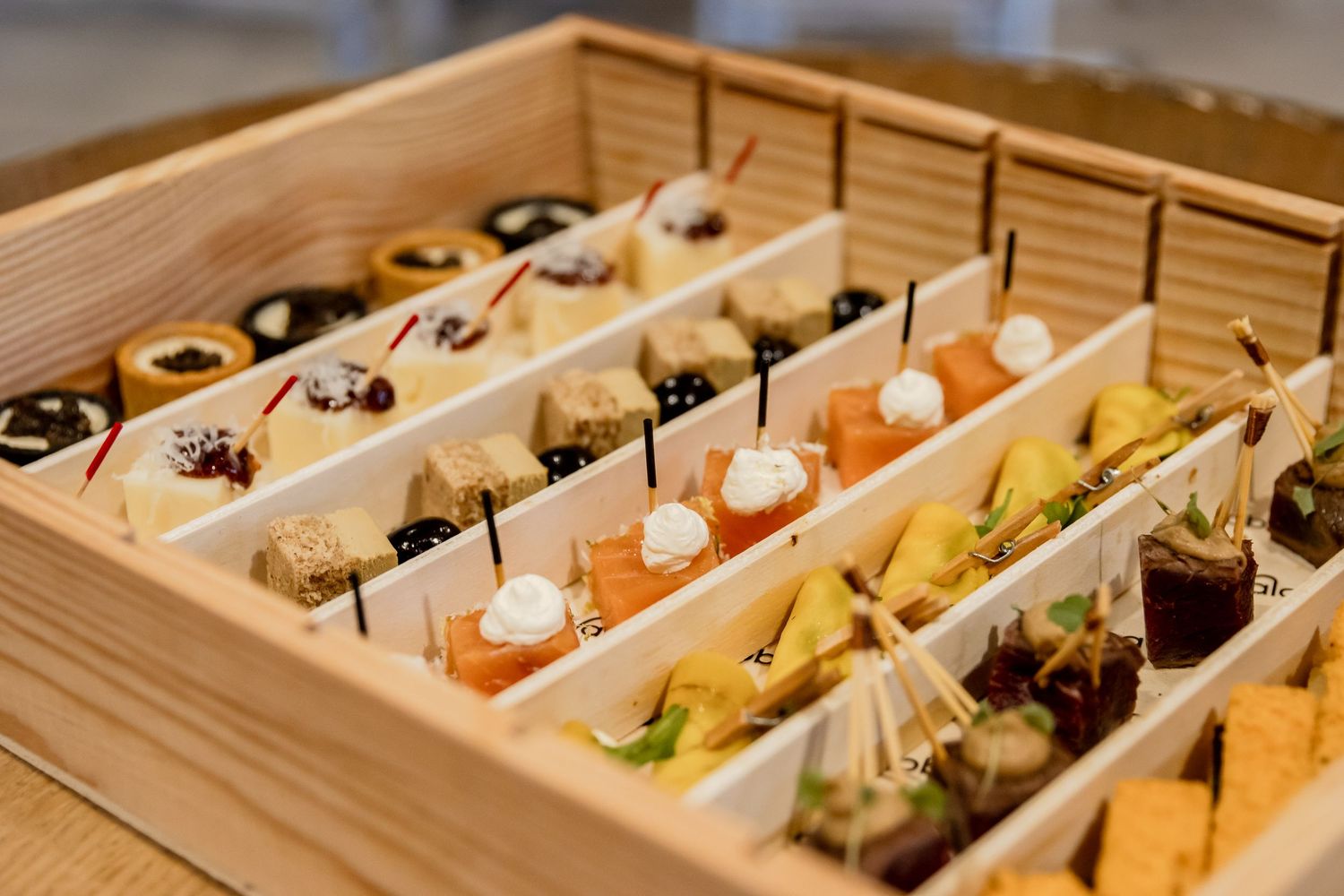 Elegant wooden box with assorted gourmet appetizers and canapes arranged in neat rows for catering or event service.
