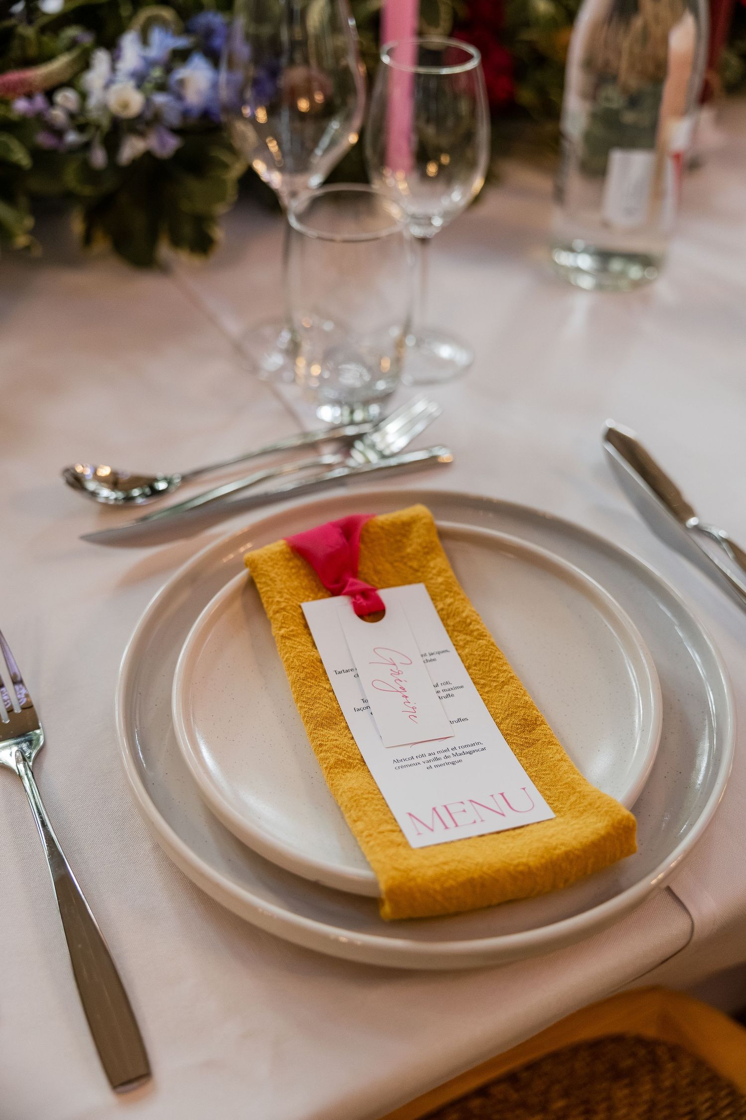 Elegant wedding place setting with yellow napkin, menu card, and crystal glassware on white tablecloth.