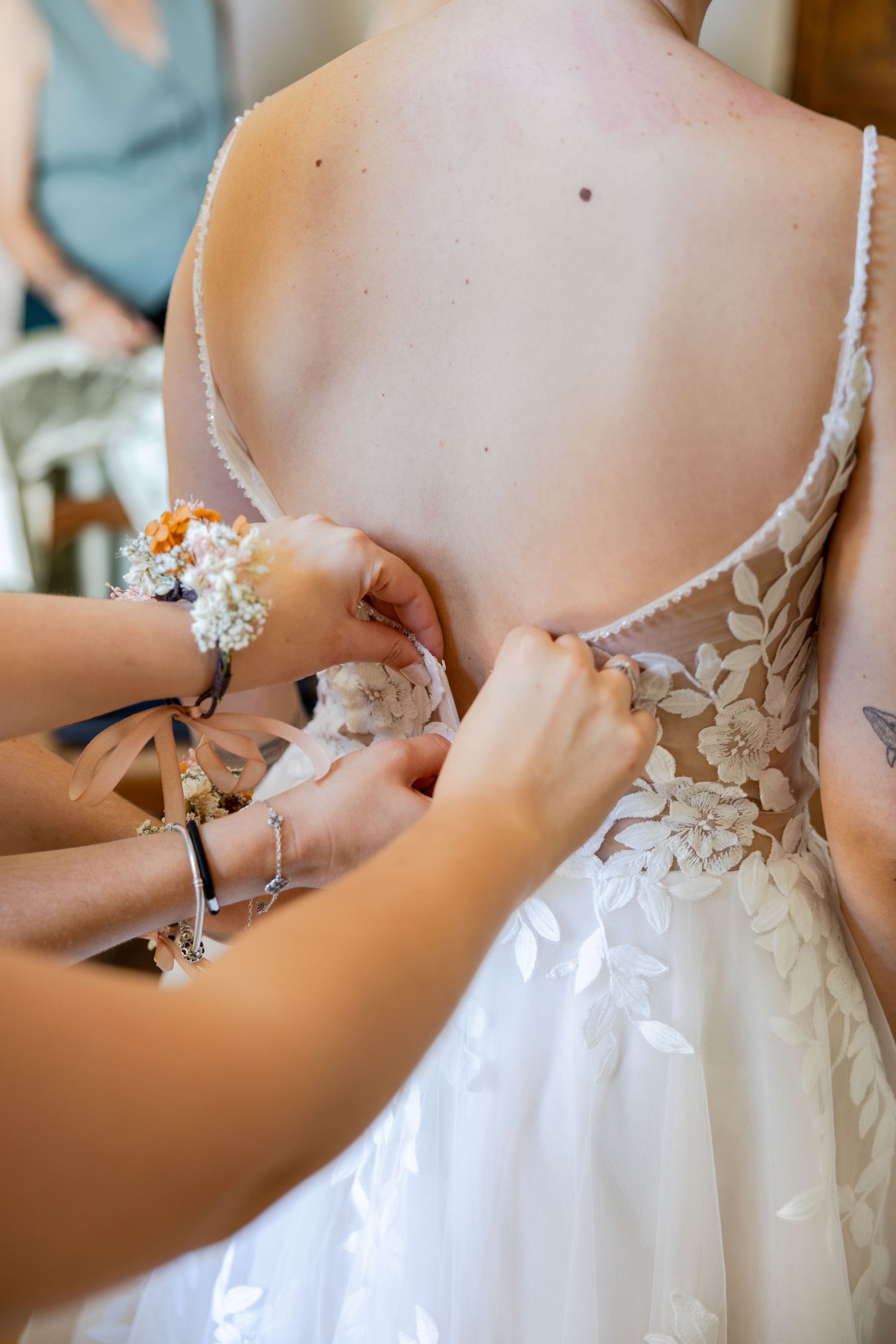 Bridesmaids fastening the back of a white lace wedding dress on a bride during bridal preparations.