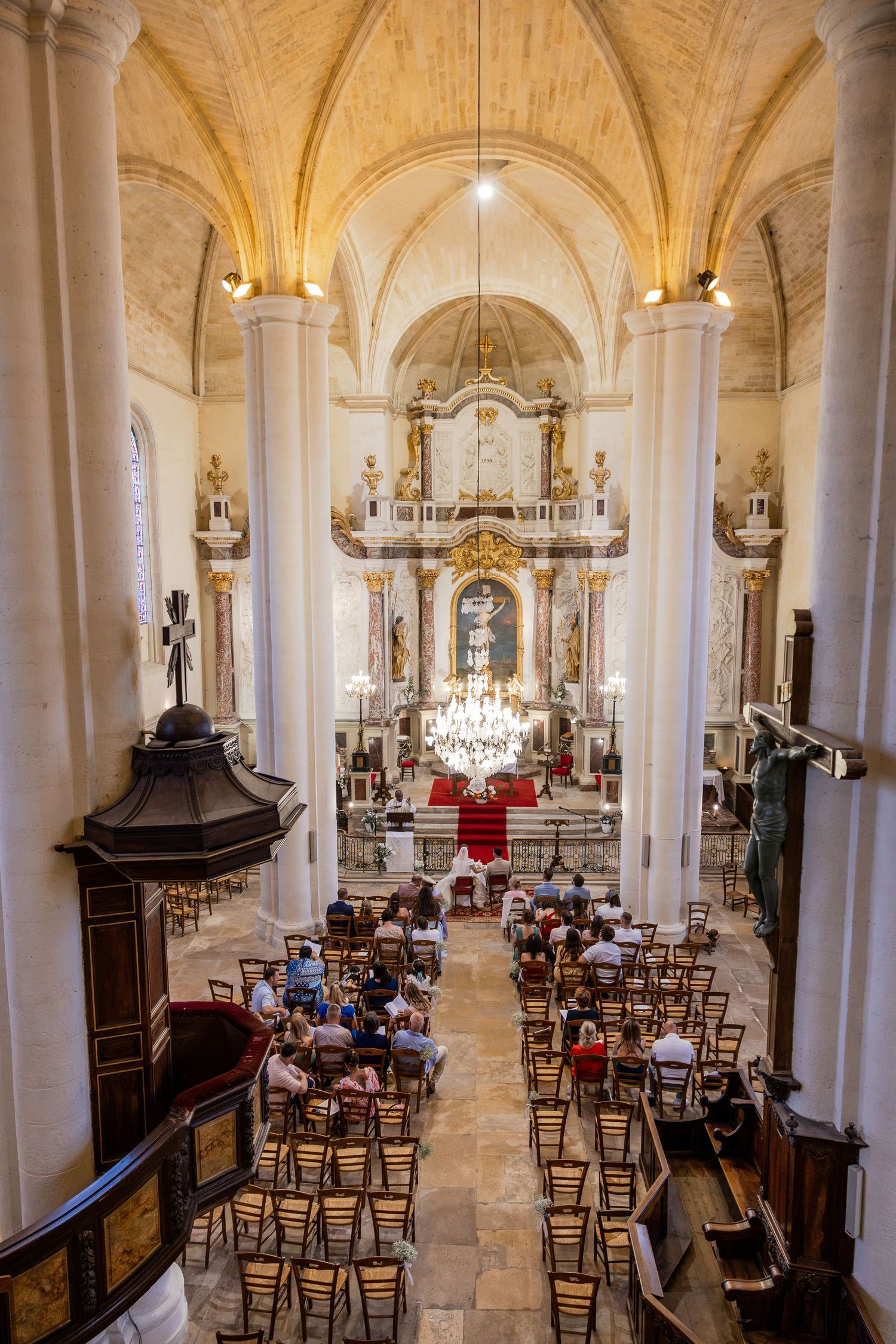 Interior of an ornate Baroque church with vaulted ceilings, golden altar, and congregation seated in wooden chairs during a service.