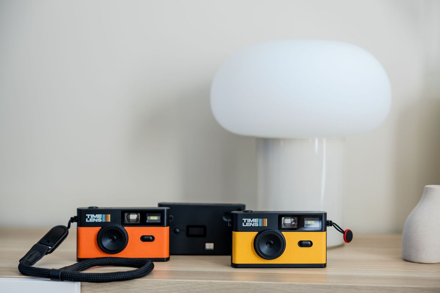 Two vintage-style orange and yellow Zenit film cameras on a wooden shelf beside a white mushroom lamp.