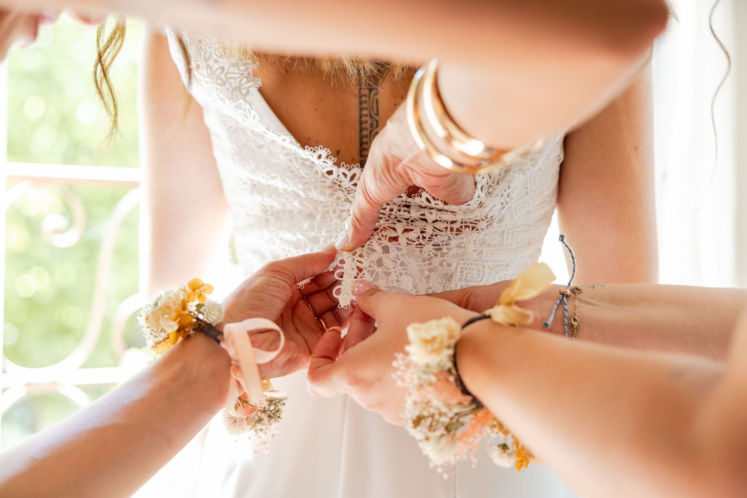 Bridesmaids fastening buttons on a white lace wedding dress with floral wrist corsages.