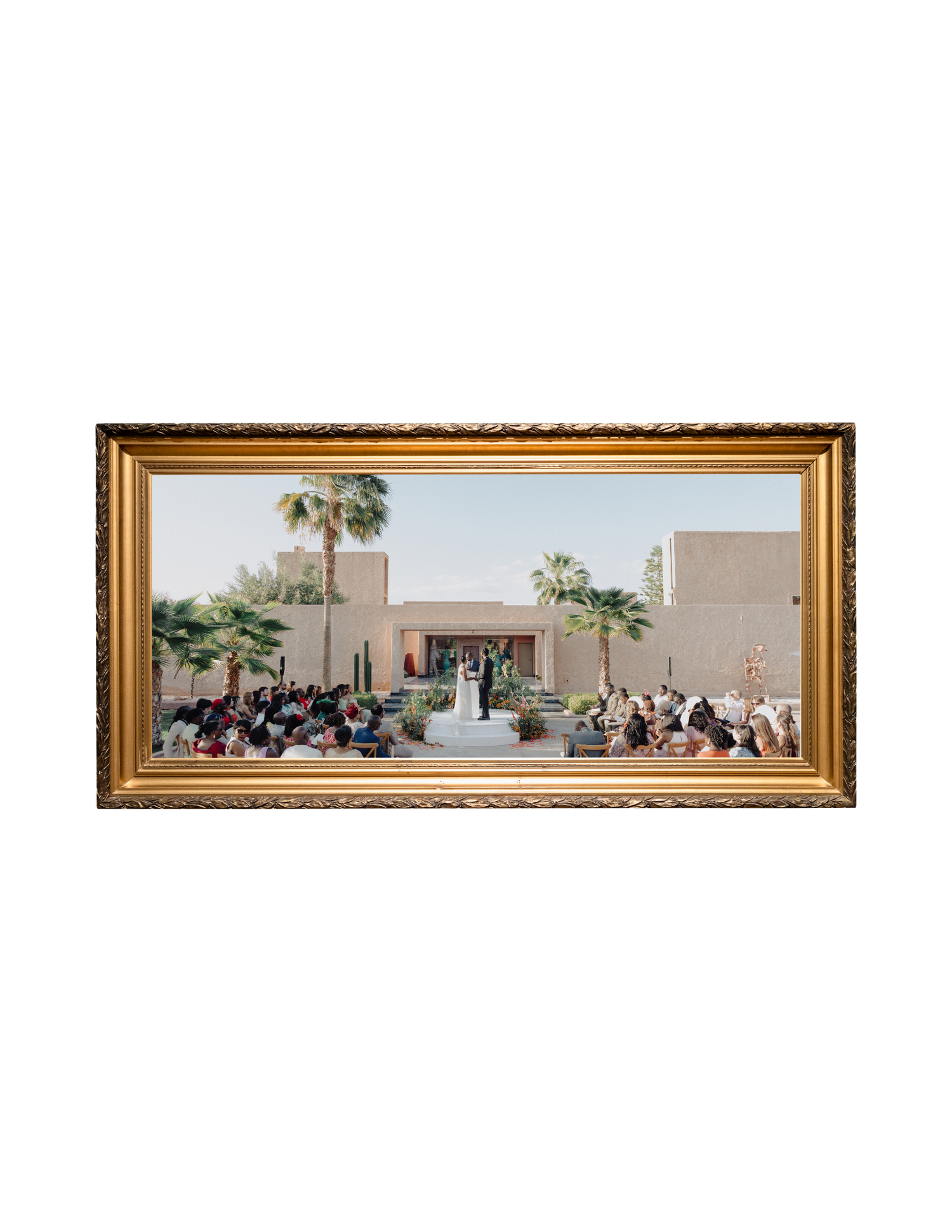 Gold ornate framed panoramic wedding ceremony photo at a desert venue with palm trees and seated guests.