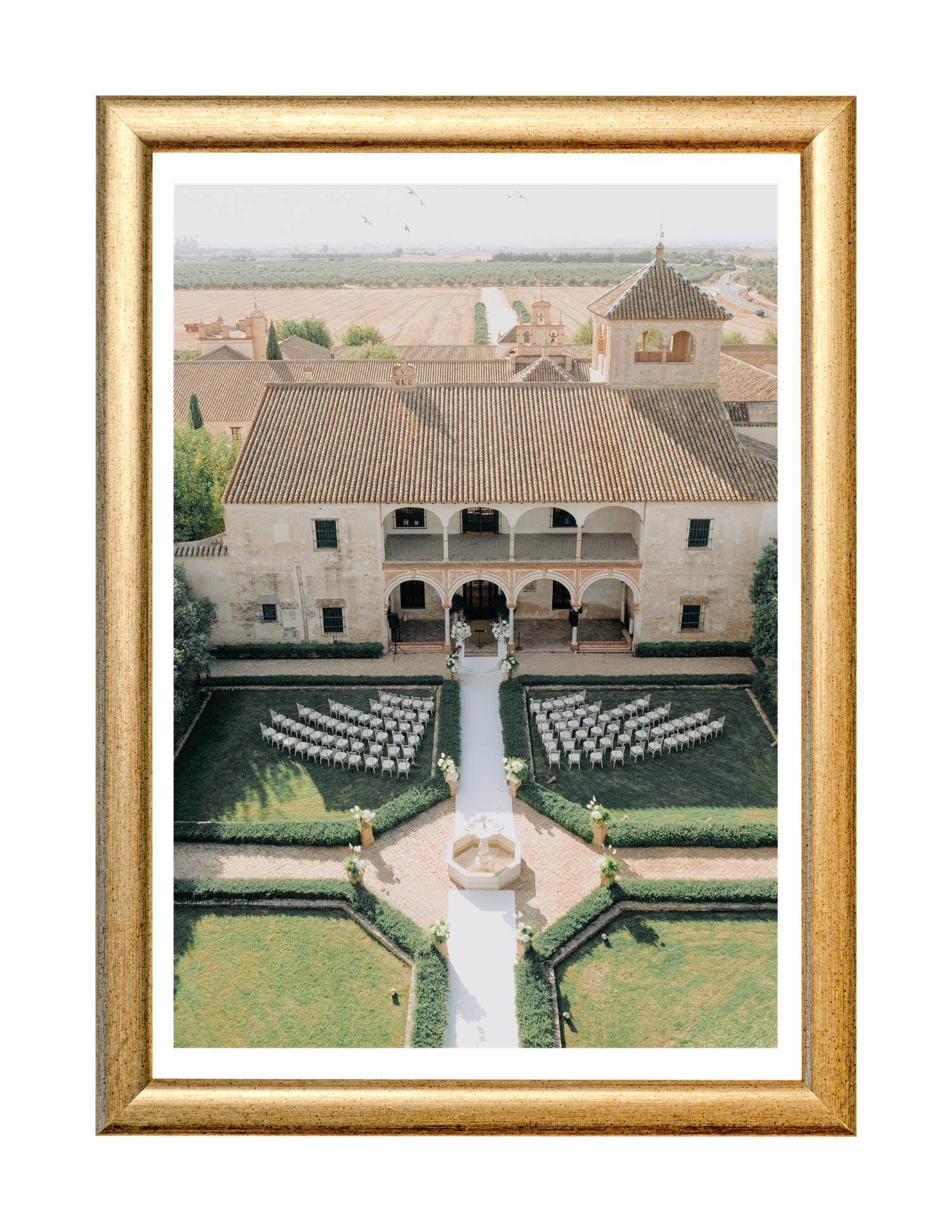Aerial view of elegant Spanish villa wedding ceremony with white chairs arranged in courtyard garden with fountain.