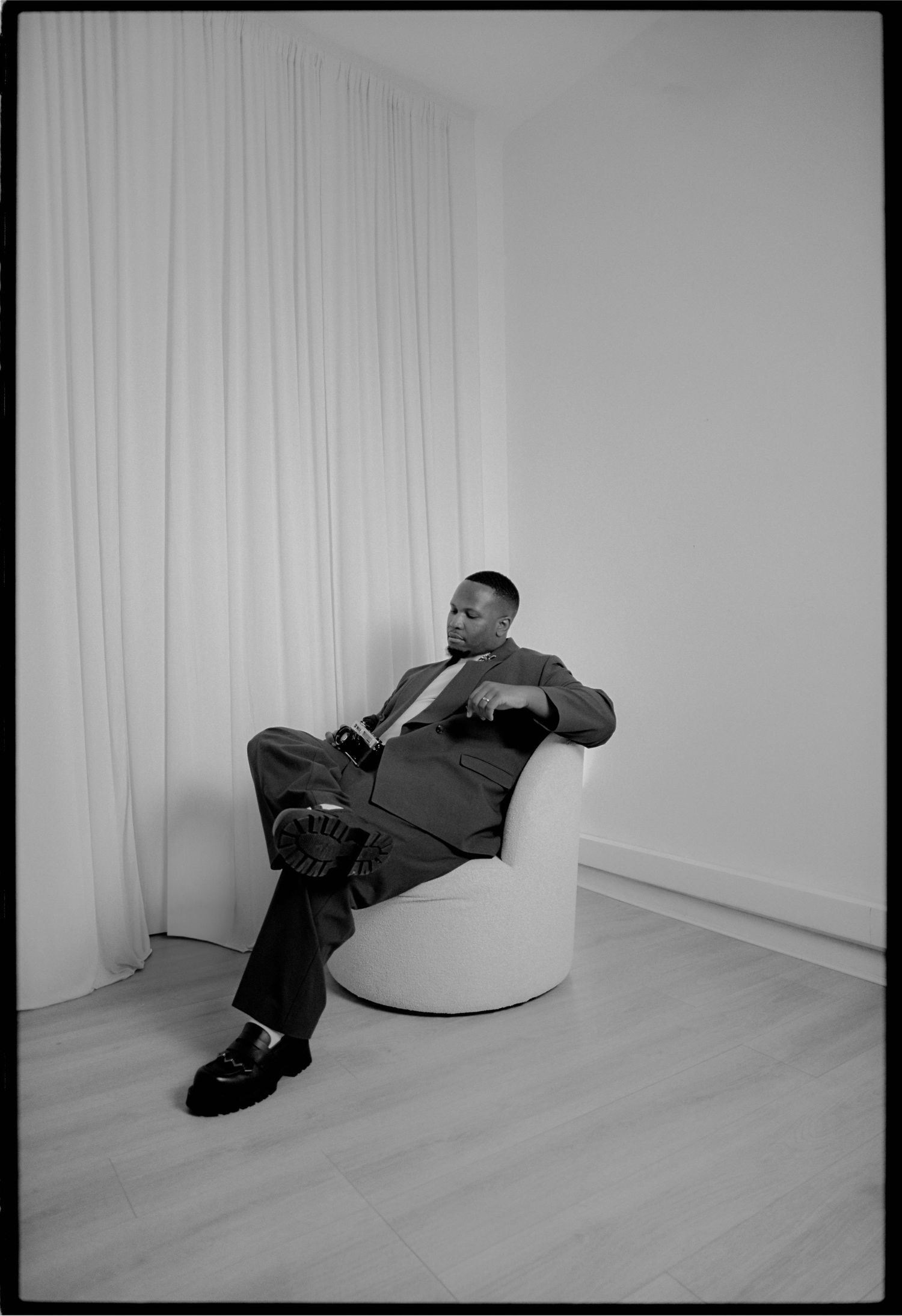 Black and white photo series showing a person in dark clothing reclining in a minimalist white room setting.