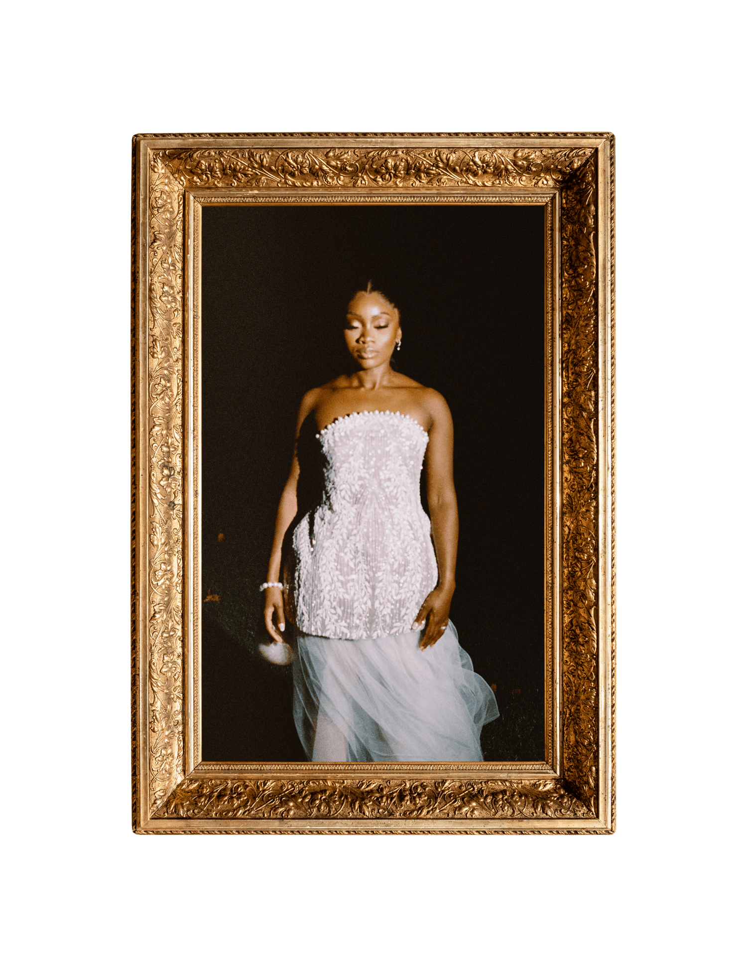 A Black woman in a white strapless lace gown posed elegantly inside an ornate gold picture frame.