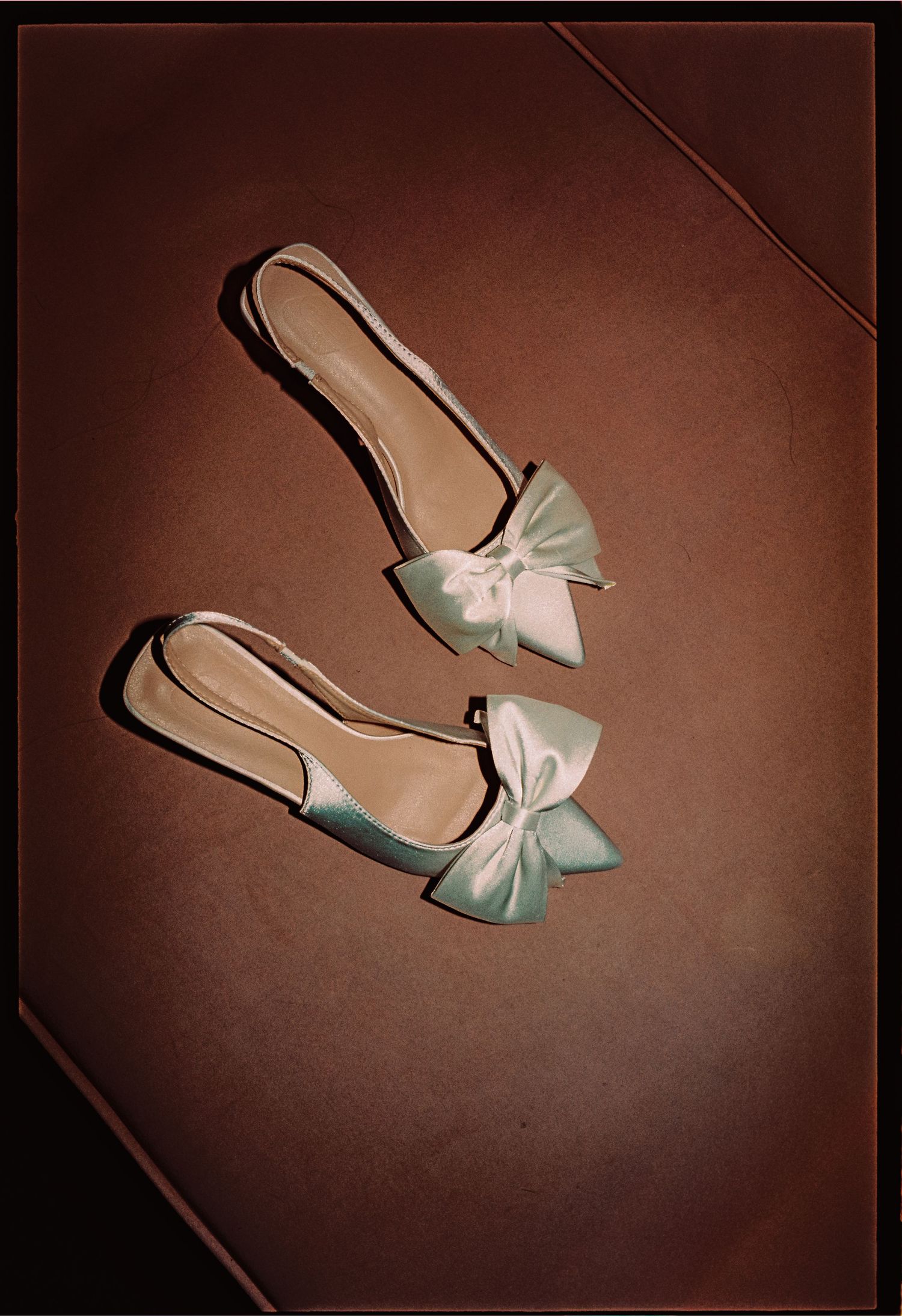 Elegant light mint green satin ballet flats with bow detail on brown surface.