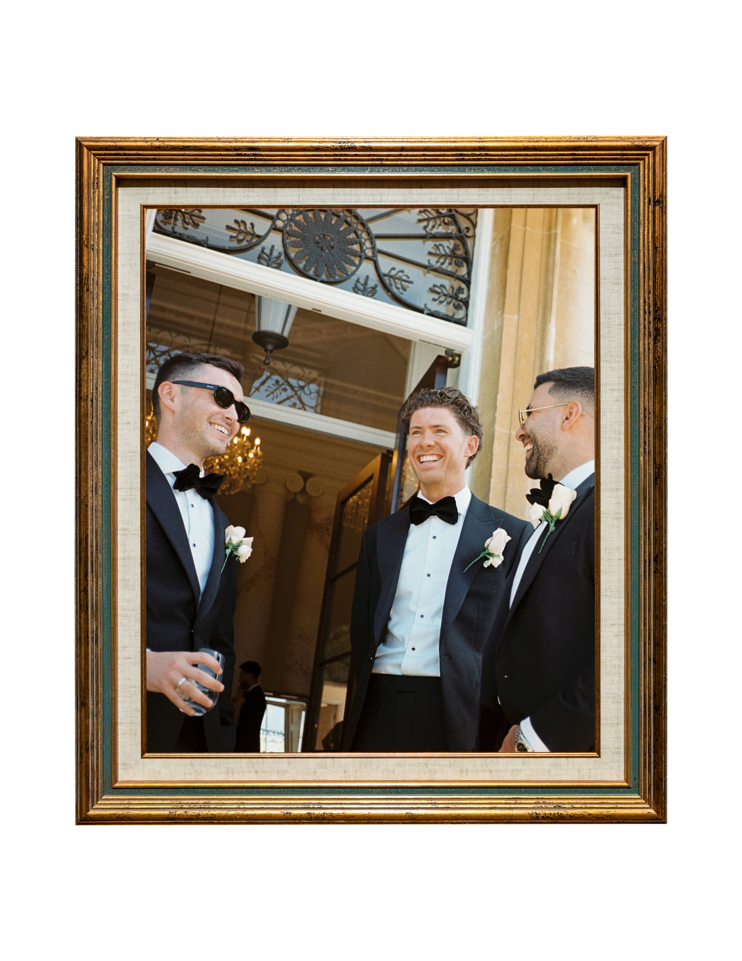 Three groomsmen in black tuxedos with bow ties laugh together at a wedding venue.