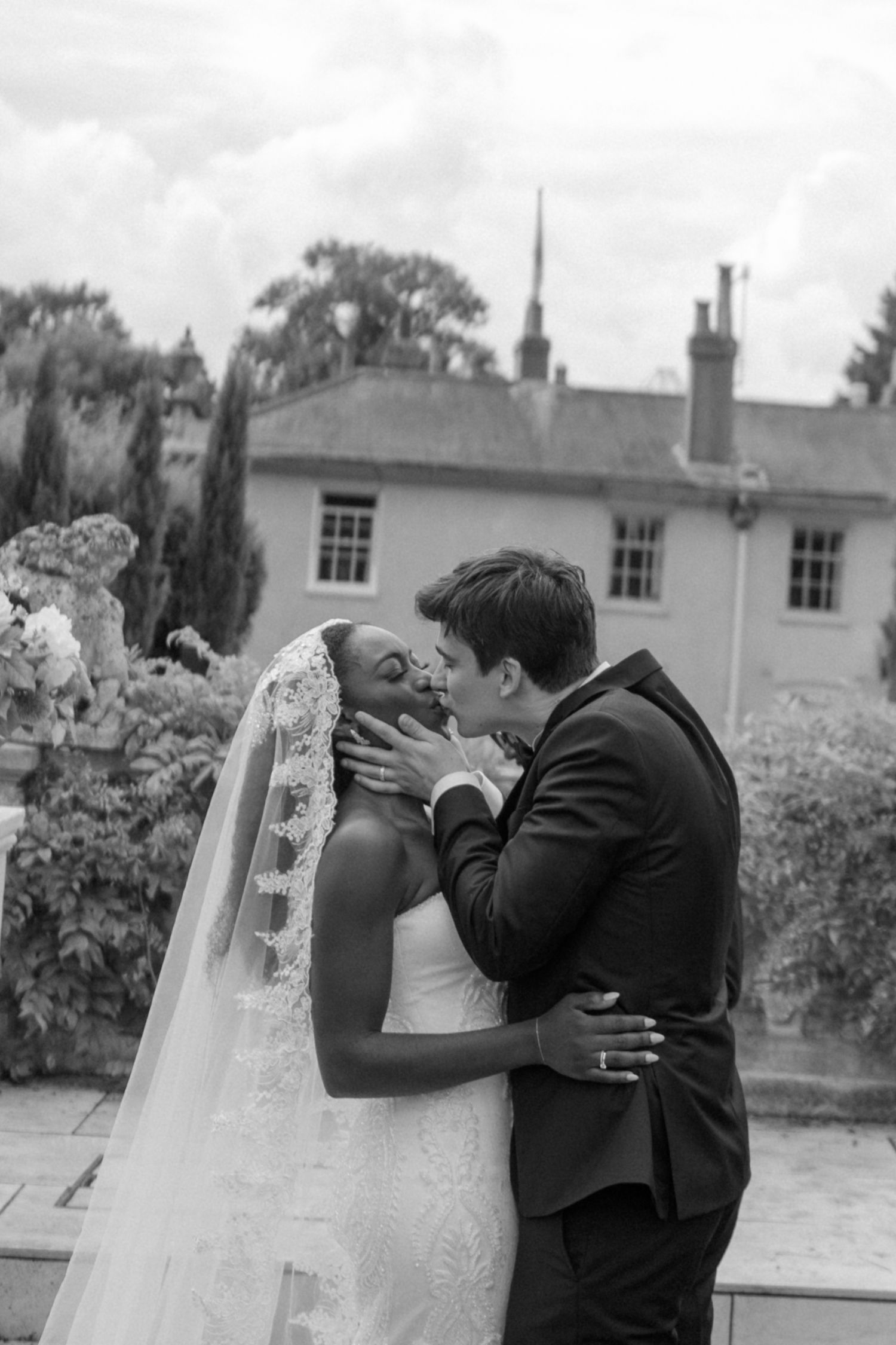 Black and white photo of a bride and groom sharing their first kiss at an outdoor wedding venue.
