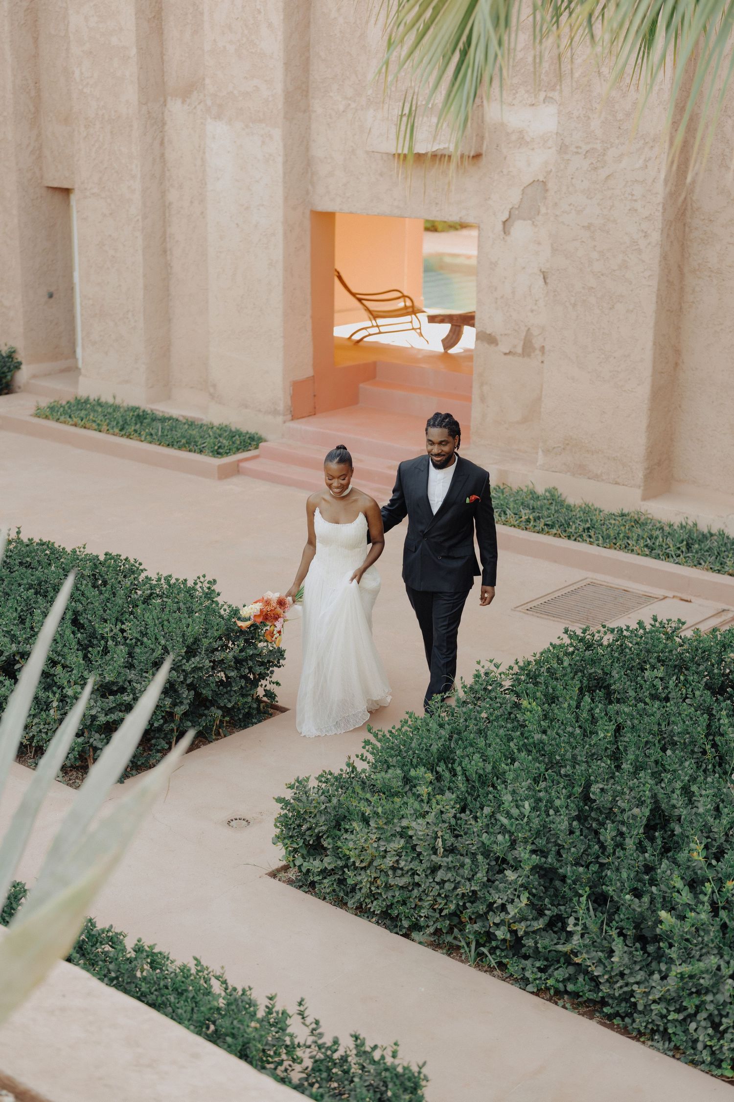 Bride and groom walking hand in hand through a manicured garden courtyard at a luxury wedding venue.