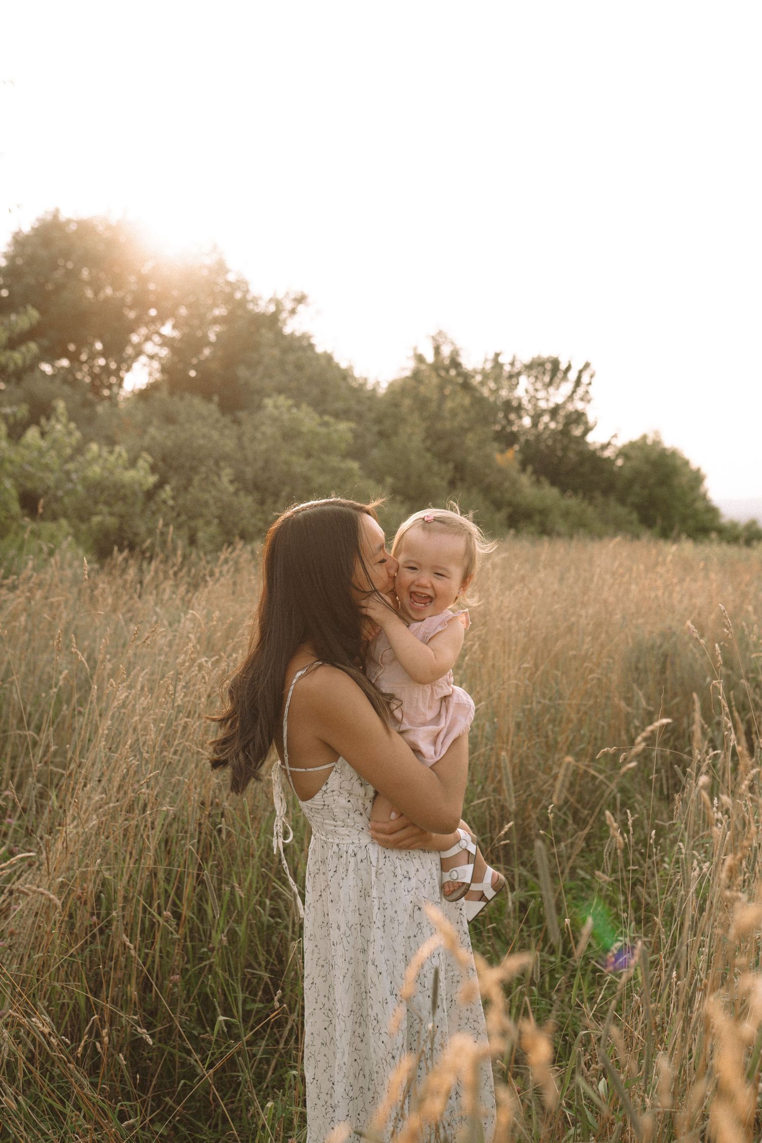 Joyful embrace between parent and child in sunlit field of tall grass.