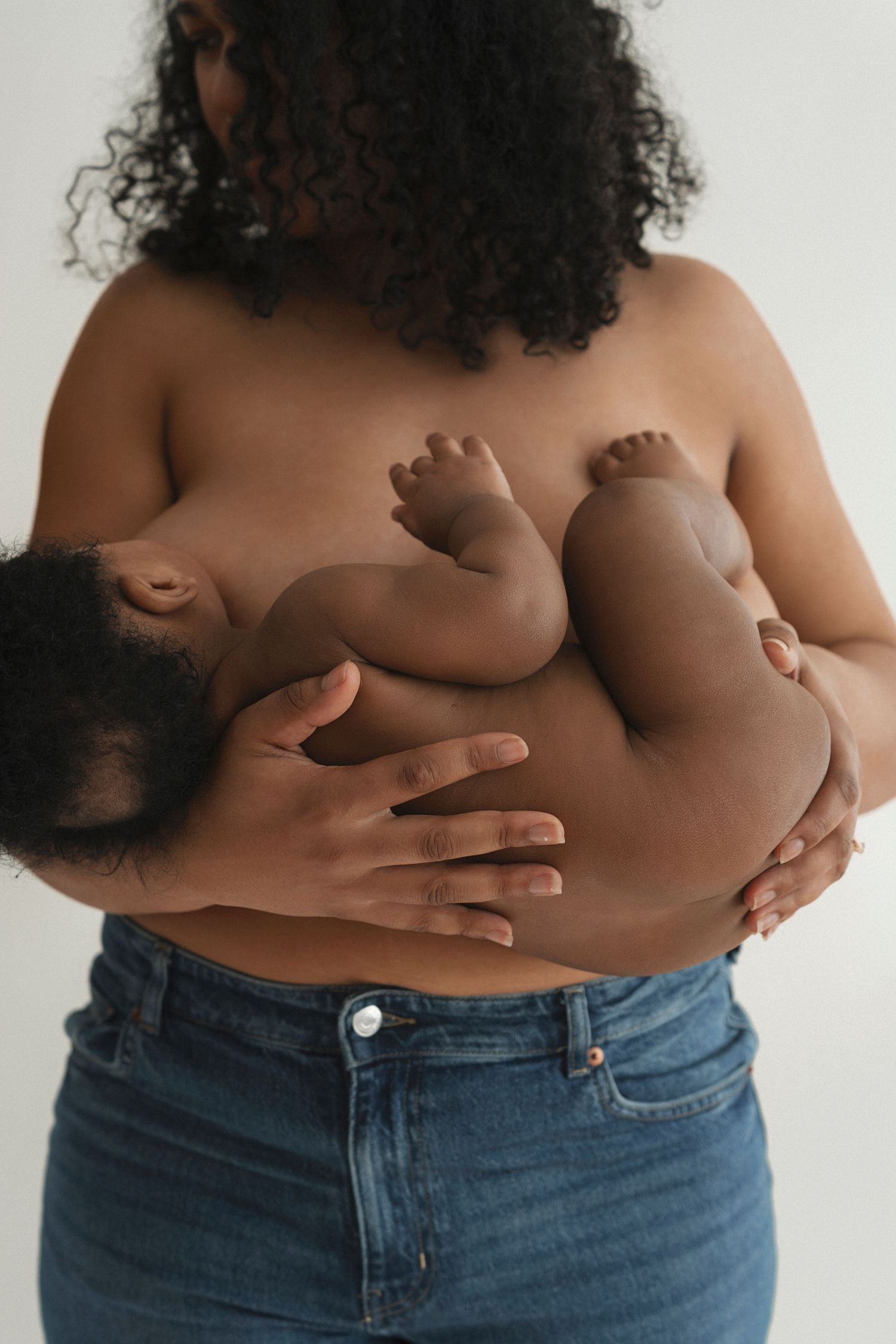 Parent in blue jeans holding sleeping infant against bare skin in tender embrace.