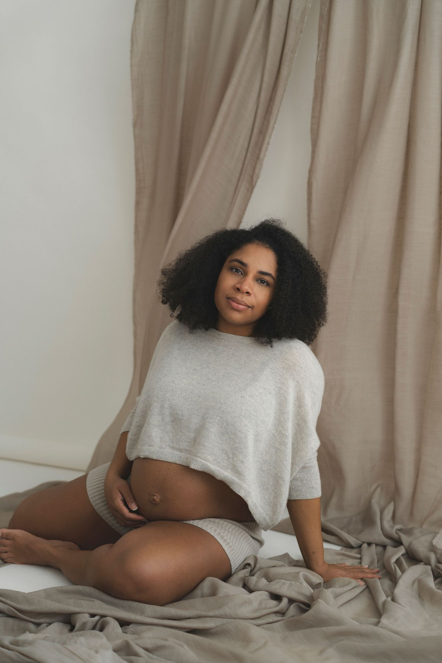 Relaxed maternity boudoir photo with soft lighting and beige drapery.