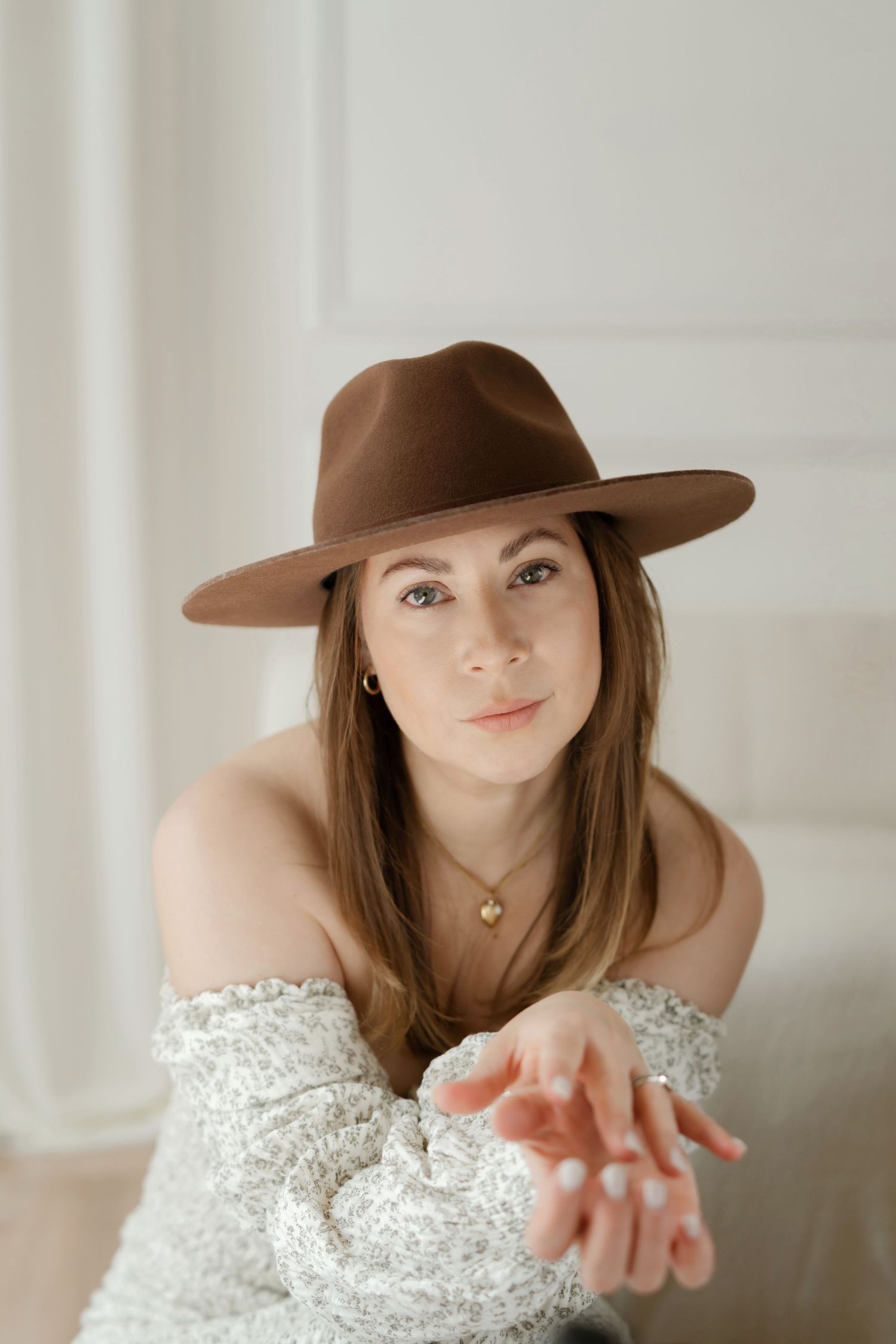 Studio portrait featuring brown fedora hat and off-shoulder white lace clothing.