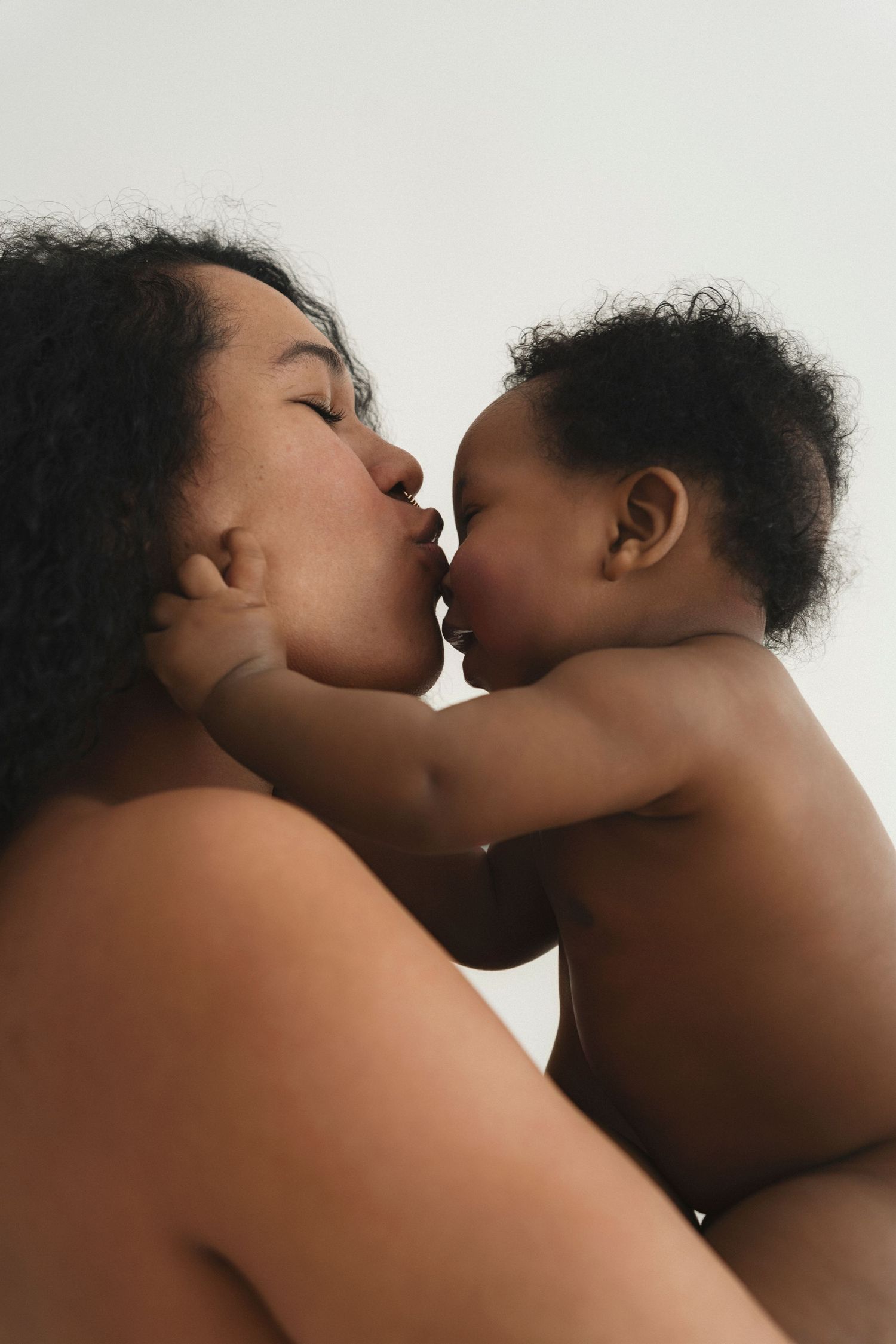 Intimate portrait of parent and baby sharing an affectionate moment against light background.