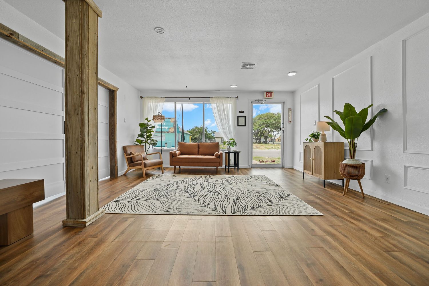 Open concept studio space with hardwood floors, white shiplap walls, wooden columns, and garden views.