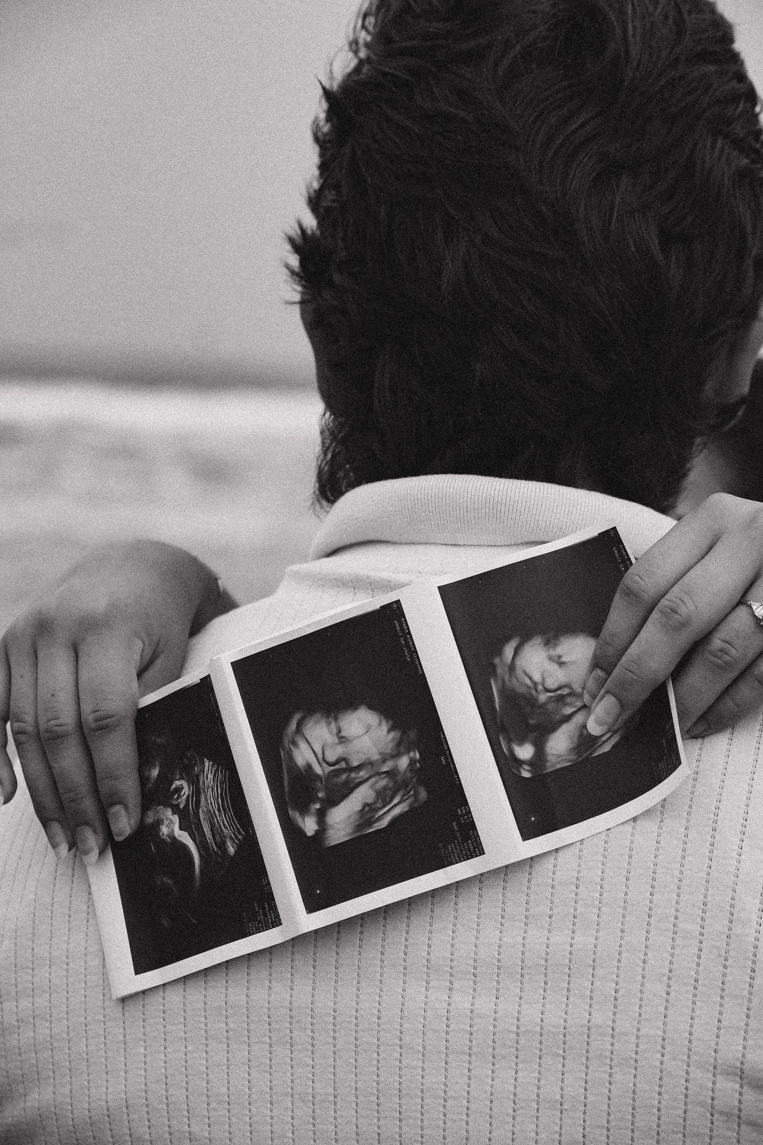 Black and white image of person holding three ultrasound photos against their back at the beach.