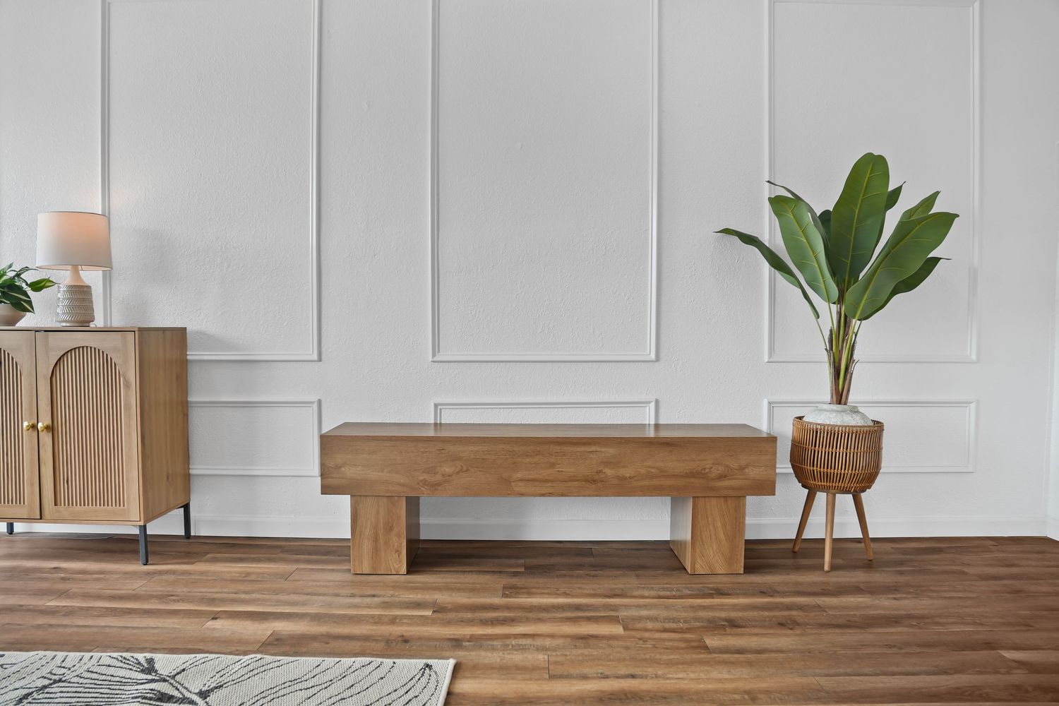 Modern rustic wooden bench centerpiece in elegant white paneled room with hardwood floors and tropical plant.