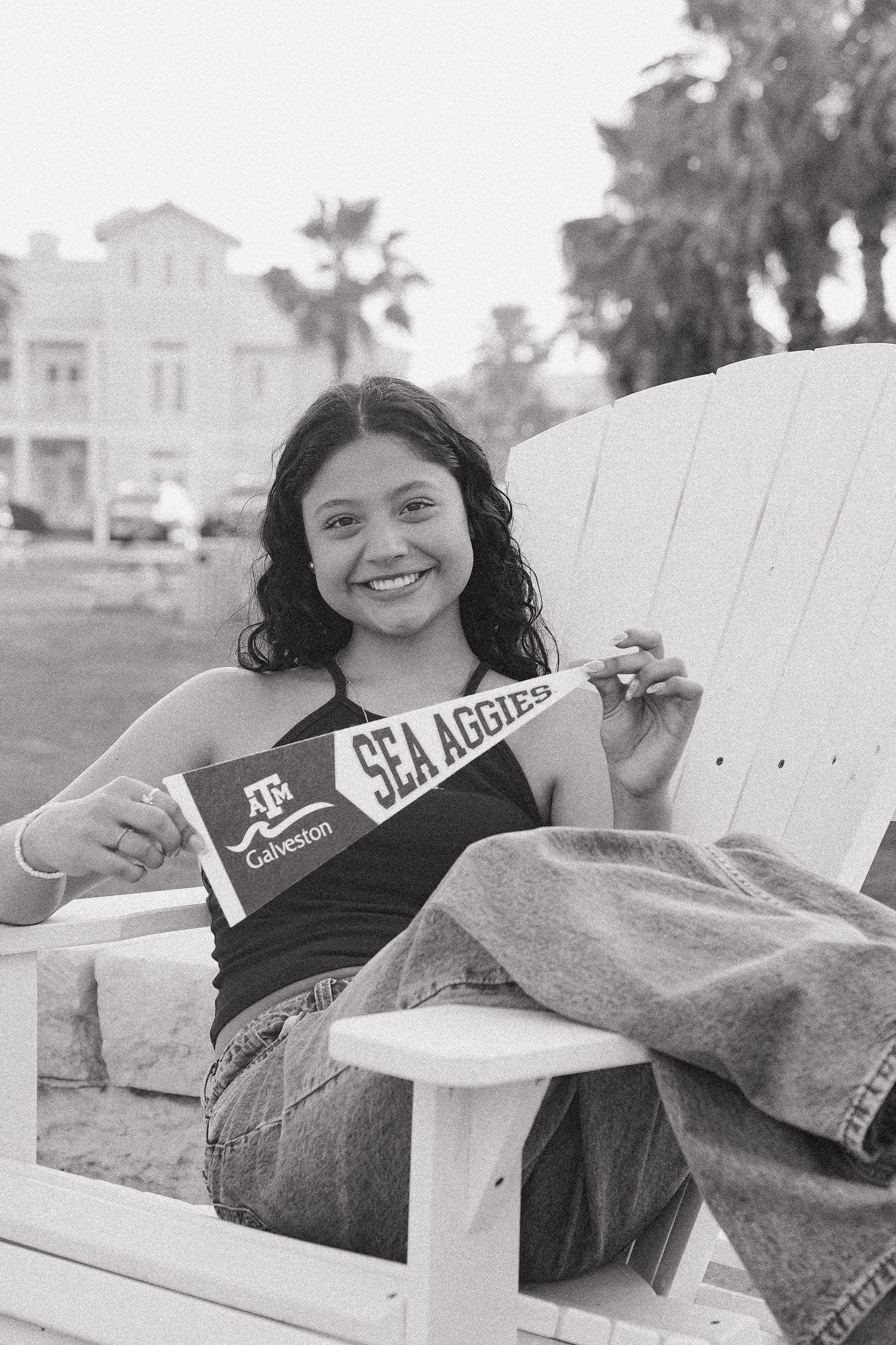Young woman smiling in chair holding Texas A&M Sea Aggies pennant flag.