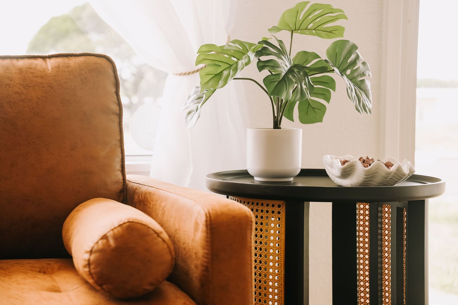 Brown leather armchair with cane detail beside a dark side table with monstera plant in white pot.