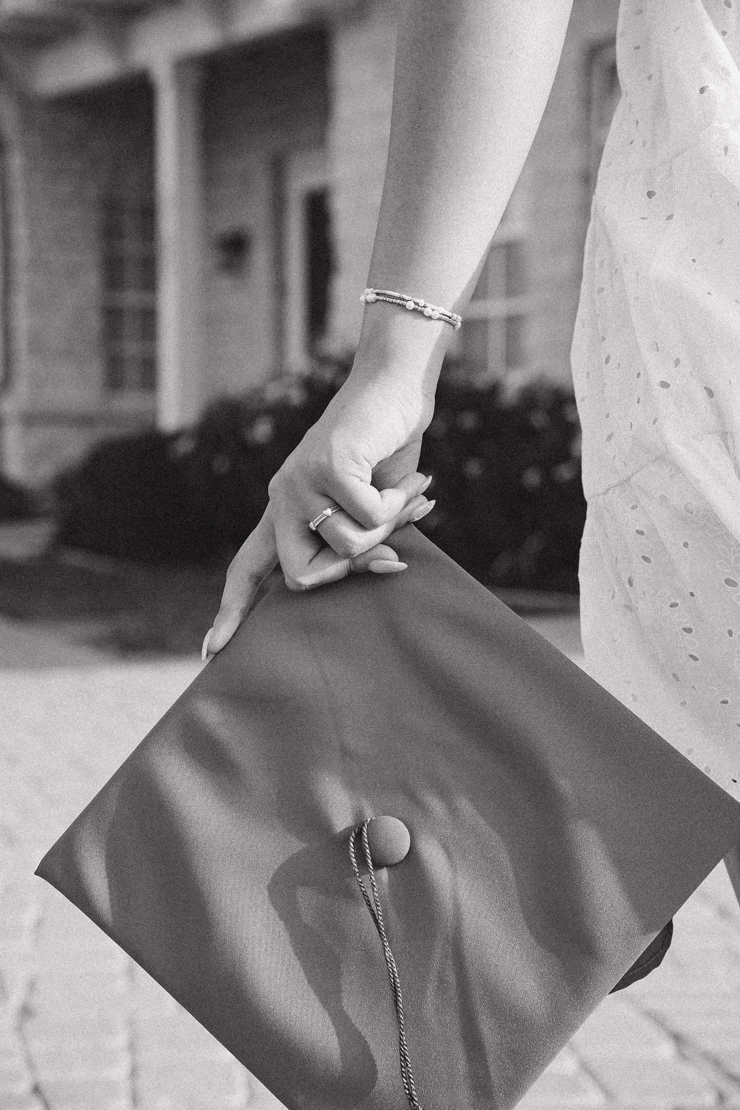 Black and white photo of woman holding graduation cap by her side.