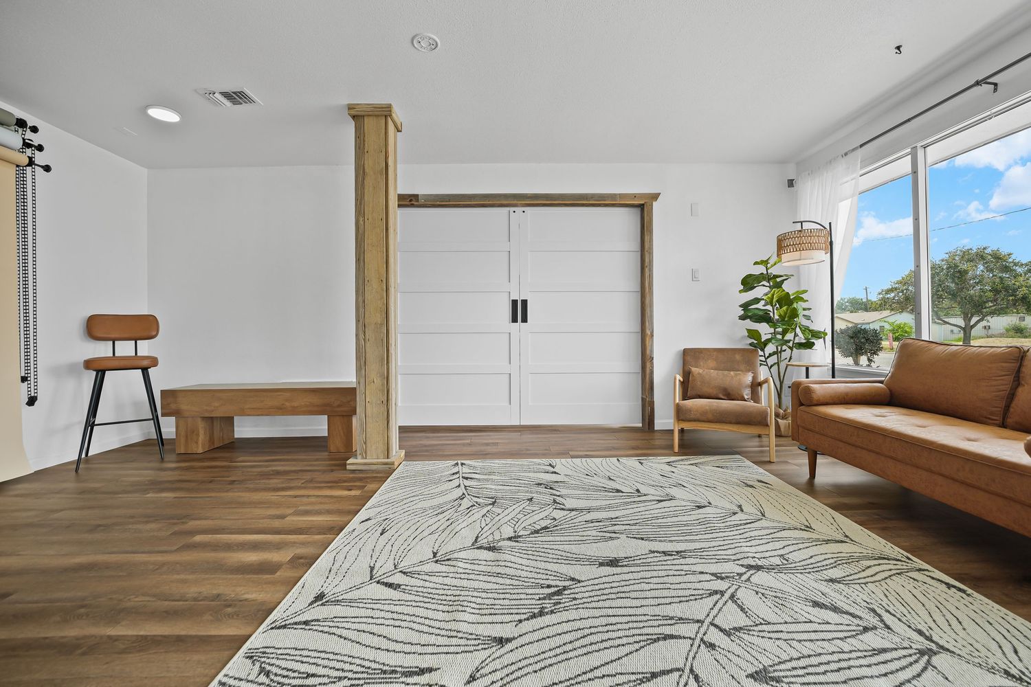 Spacious entryway with white double doors, wooden columns, brown leather sofa, and herringbone hardwood flooring.