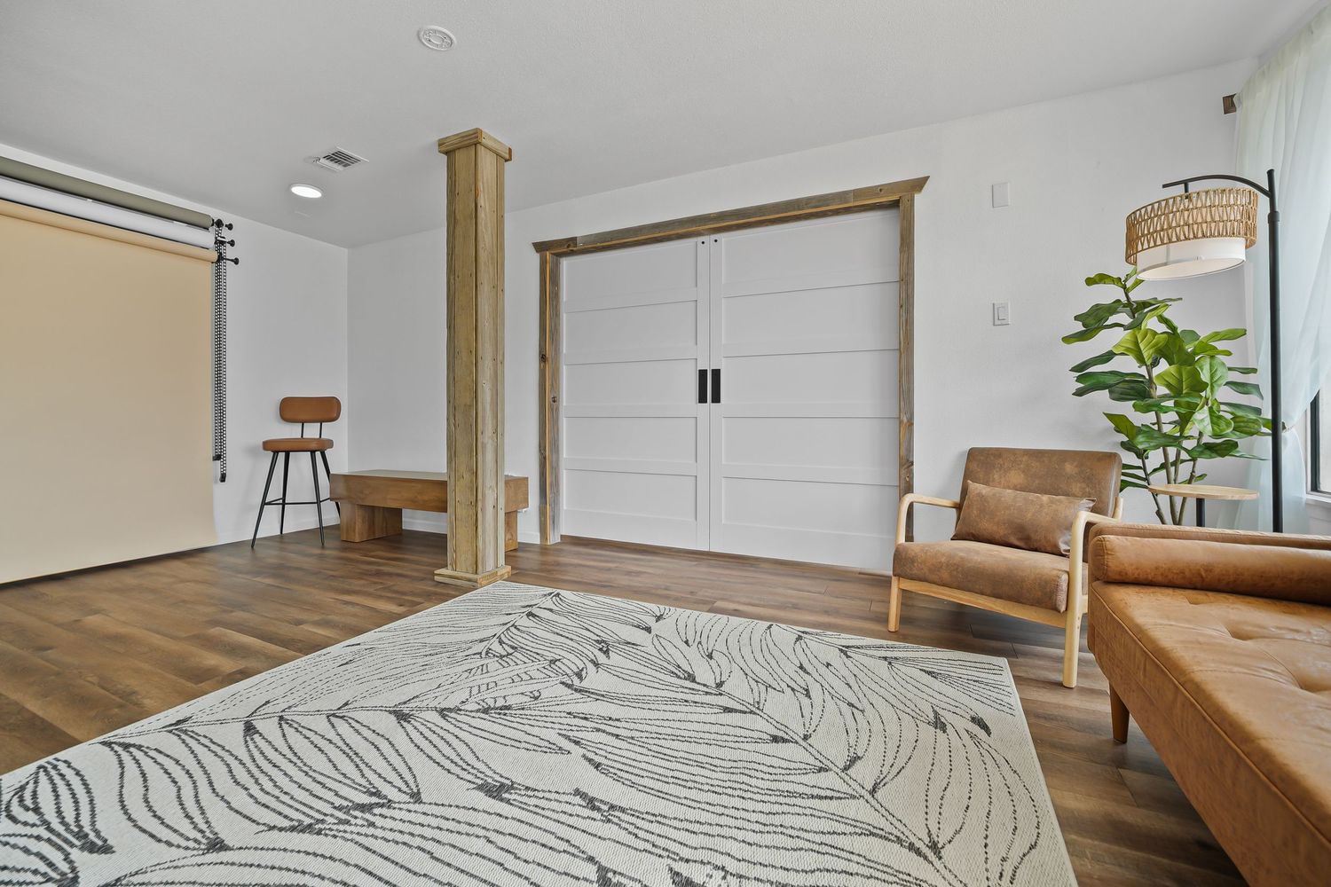 Modern living area with white double doors, wooden support column, leather seating, and stylish patterned area rug.