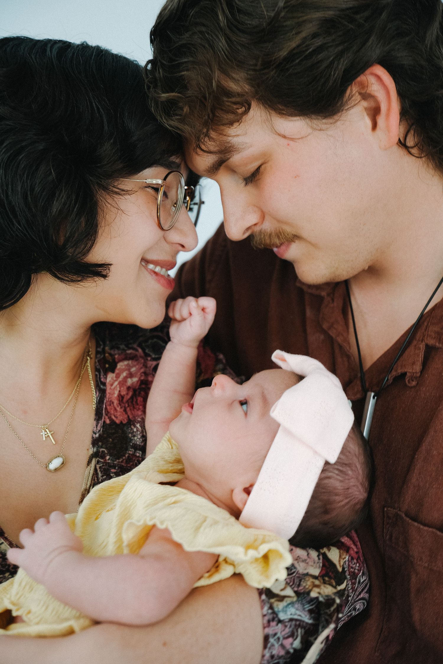Young couple smiling at each other while tenderly holding their newborn baby dressed in yellow.