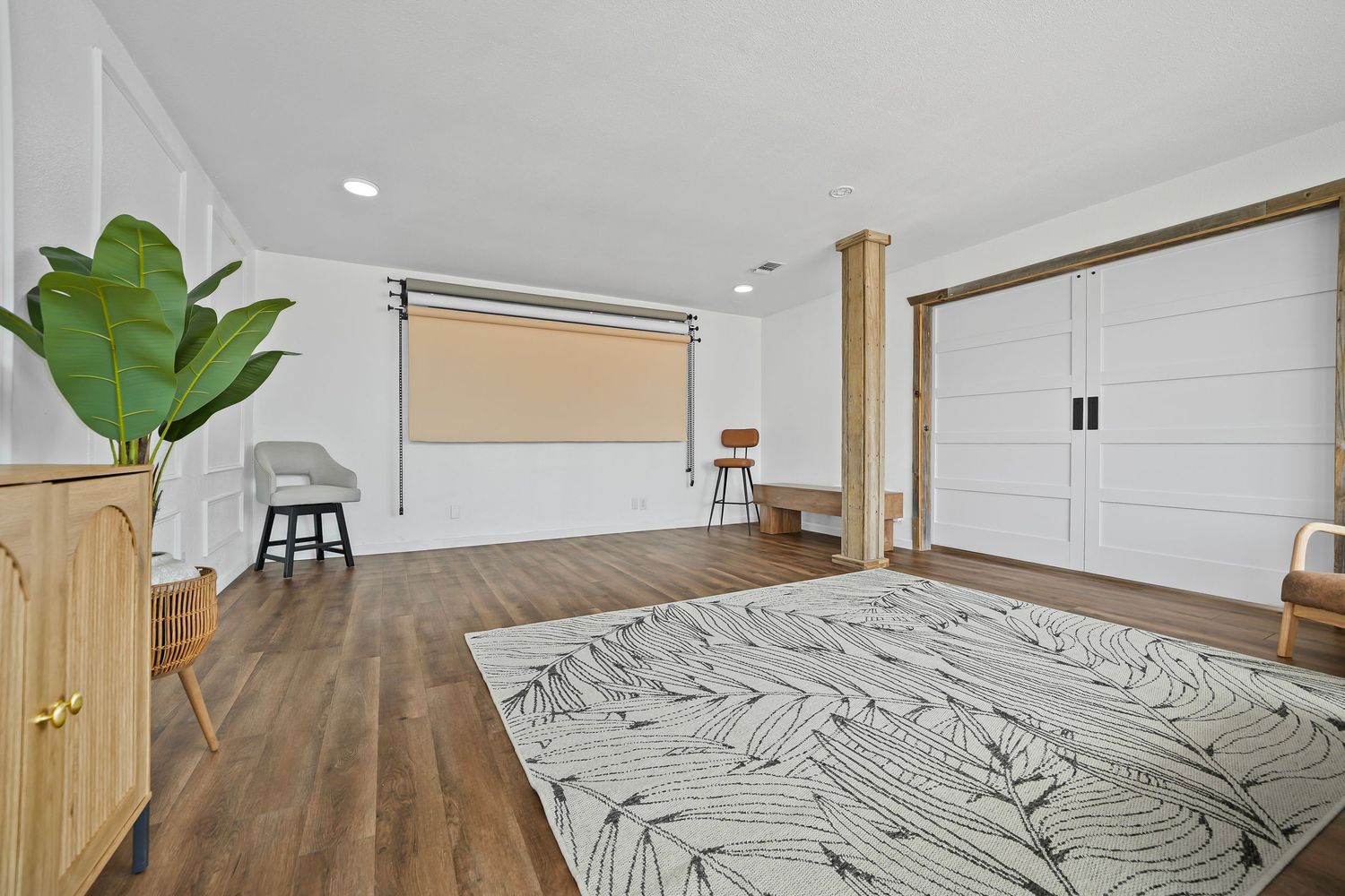 Bright open studio space with hardwood floors, white walls, leaf-print area rug, and modern furnishings.
