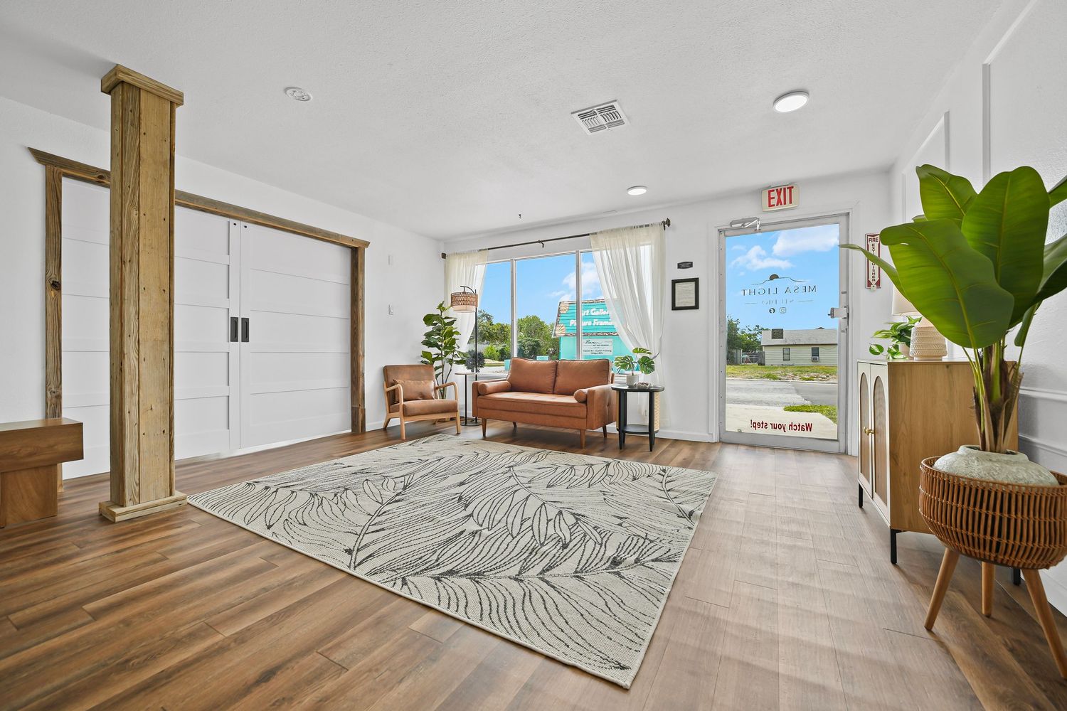 Bright modern studio interior with hardwood floors, white walls, leaf-print rug, and large glass doors.