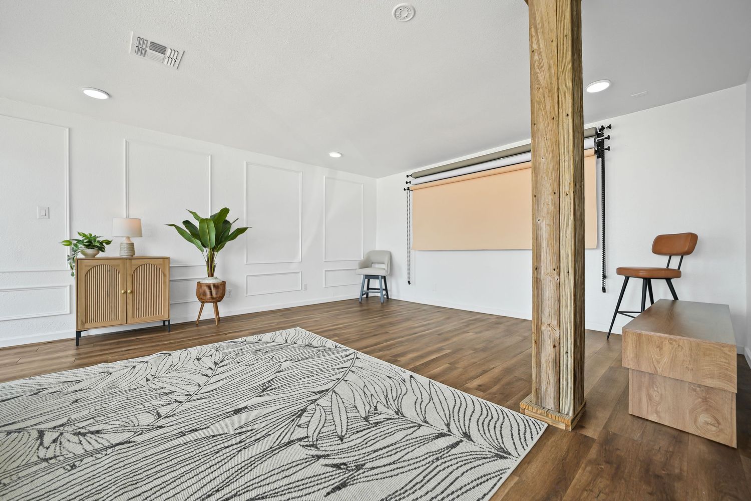 Spacious bright studio room with white wainscoting, hardwood floors, wooden column, and modern decor.