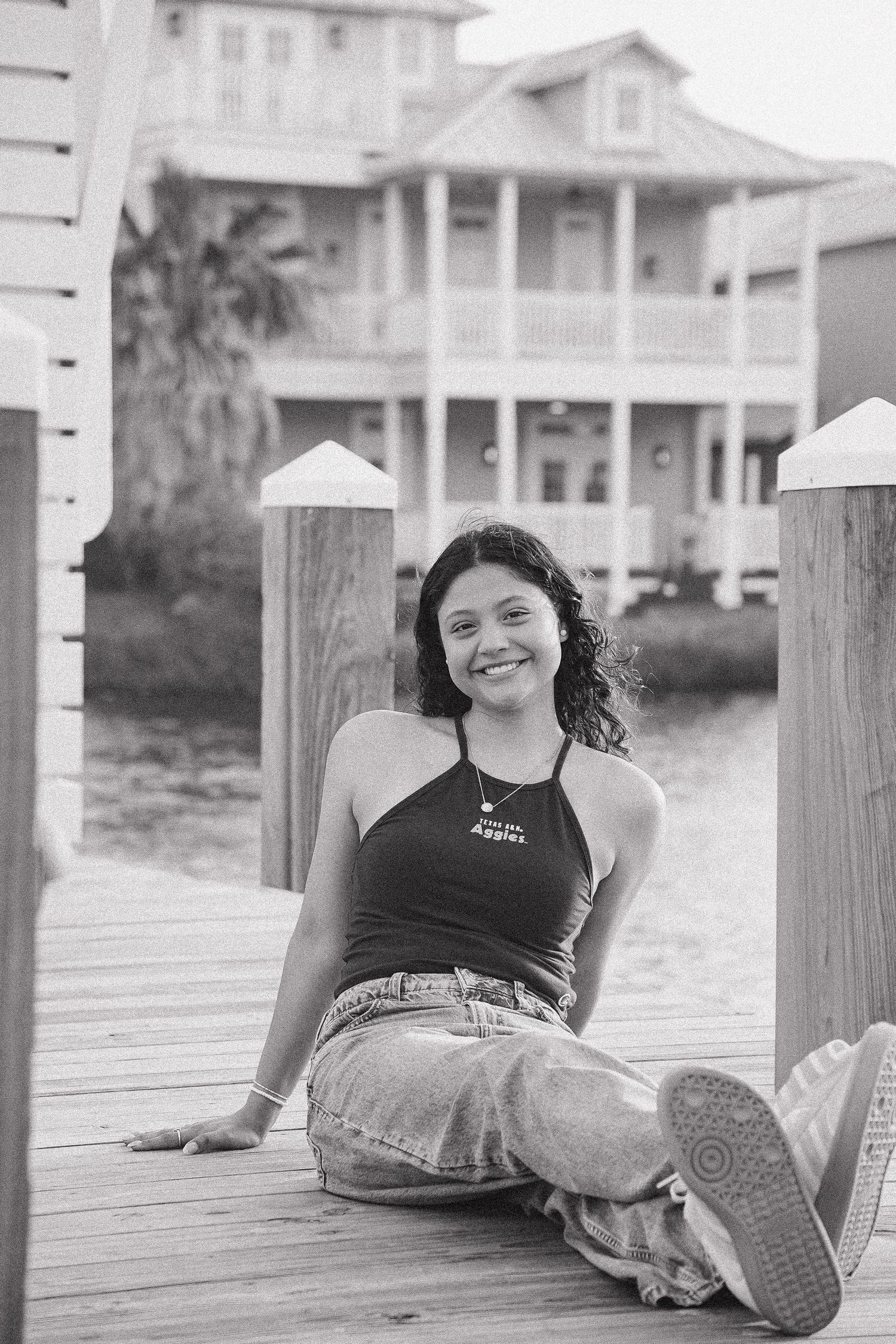 Smiling young woman sitting on wooden dock in black and white photo.