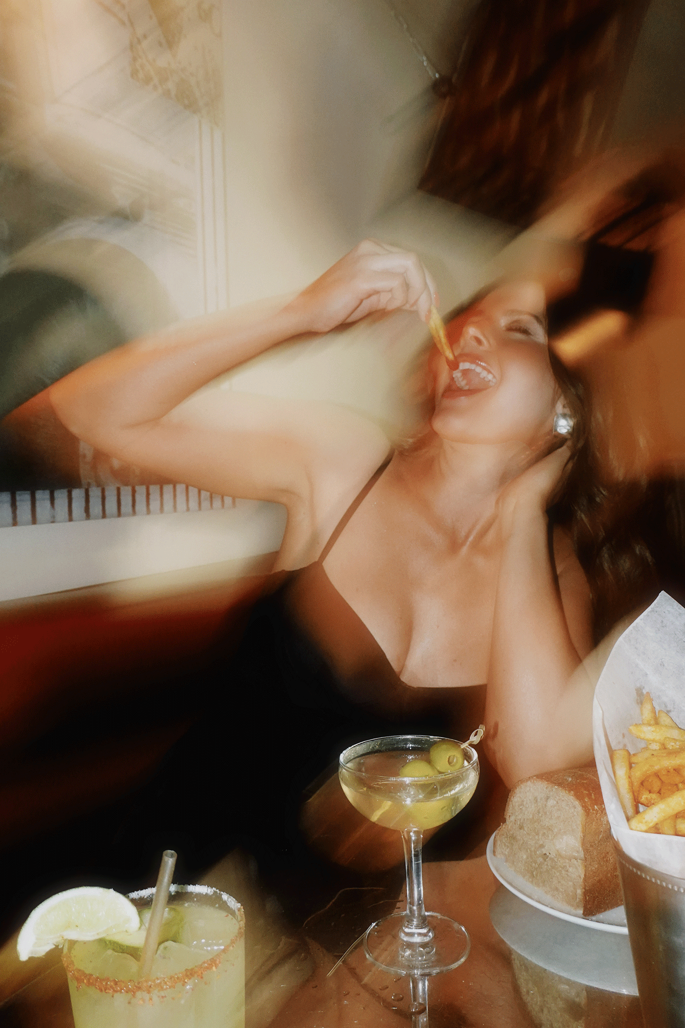 Woman laughing and enjoying drinks and fries at a bar, with motion blur creating a lively nightlife atmosphere.