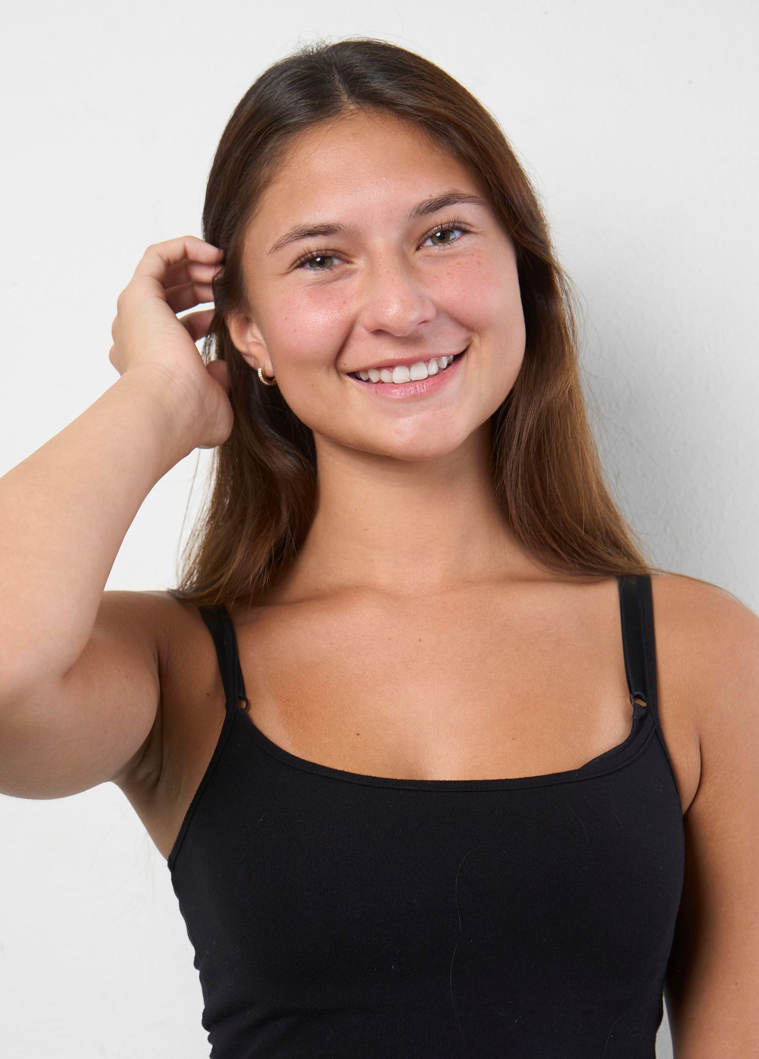 Smiling young woman with long brown hair wearing a black tank top poses against a white background.