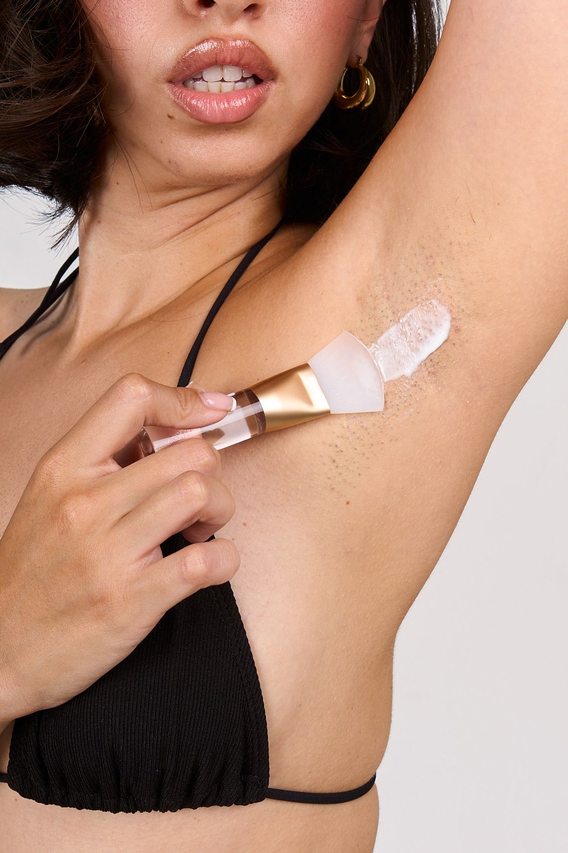 Woman applying deodorant to her underarm with applicator, wearing a black bikini top.