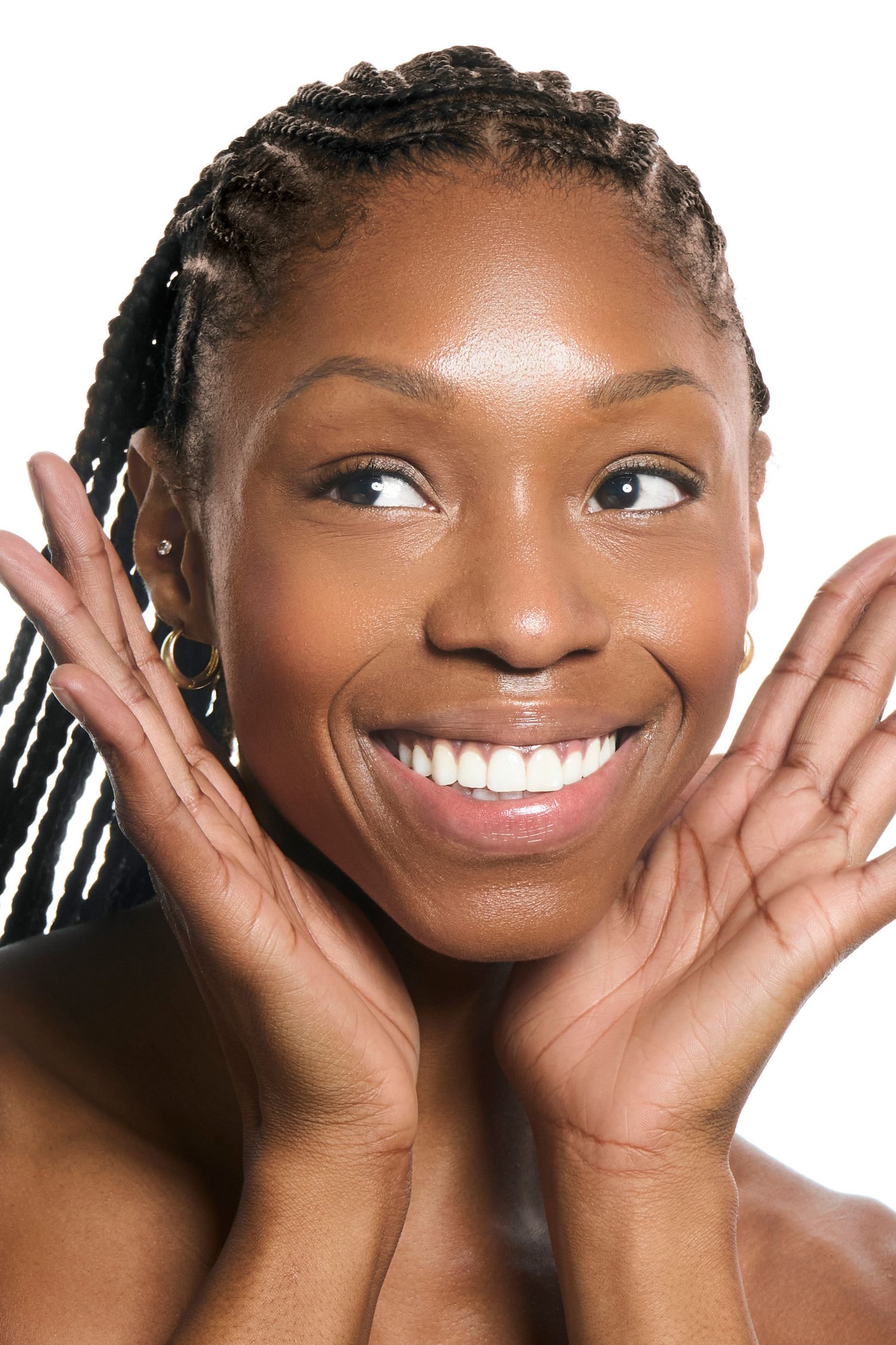 A joyful Black woman with braided hair smiles brightly, hands framing her face against a white background.