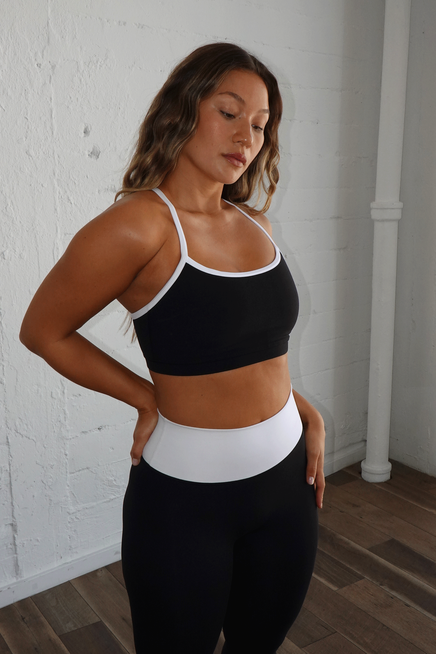 Woman wearing black sports bra with white trim and high-waisted black leggings with white waistband.