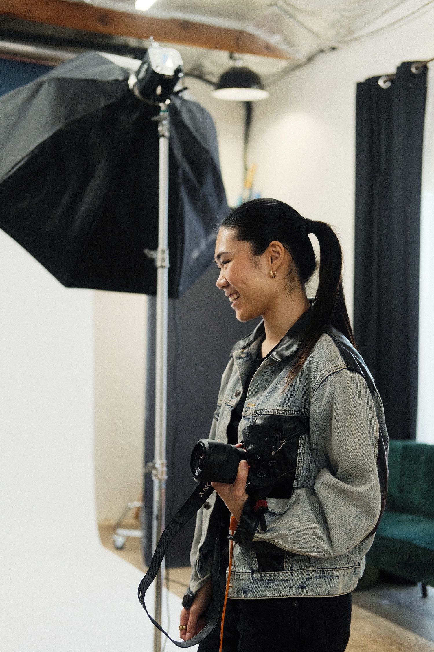 Smiling female photographer holding a DSLR camera in a professional photo studio with softbox lighting equipment.