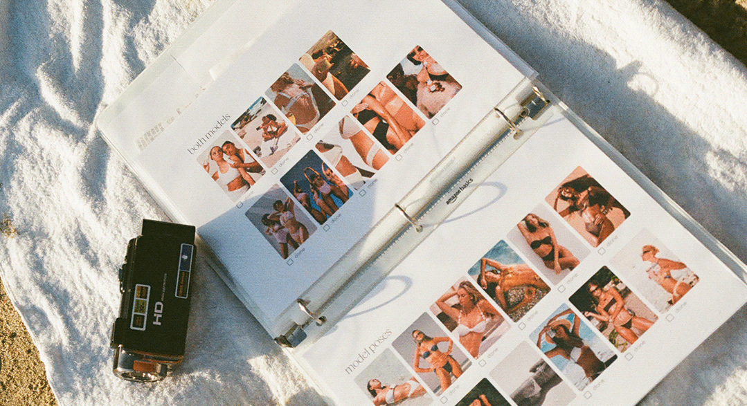 Open photo album with vacation beach pictures lying on sand next to a small black camera.