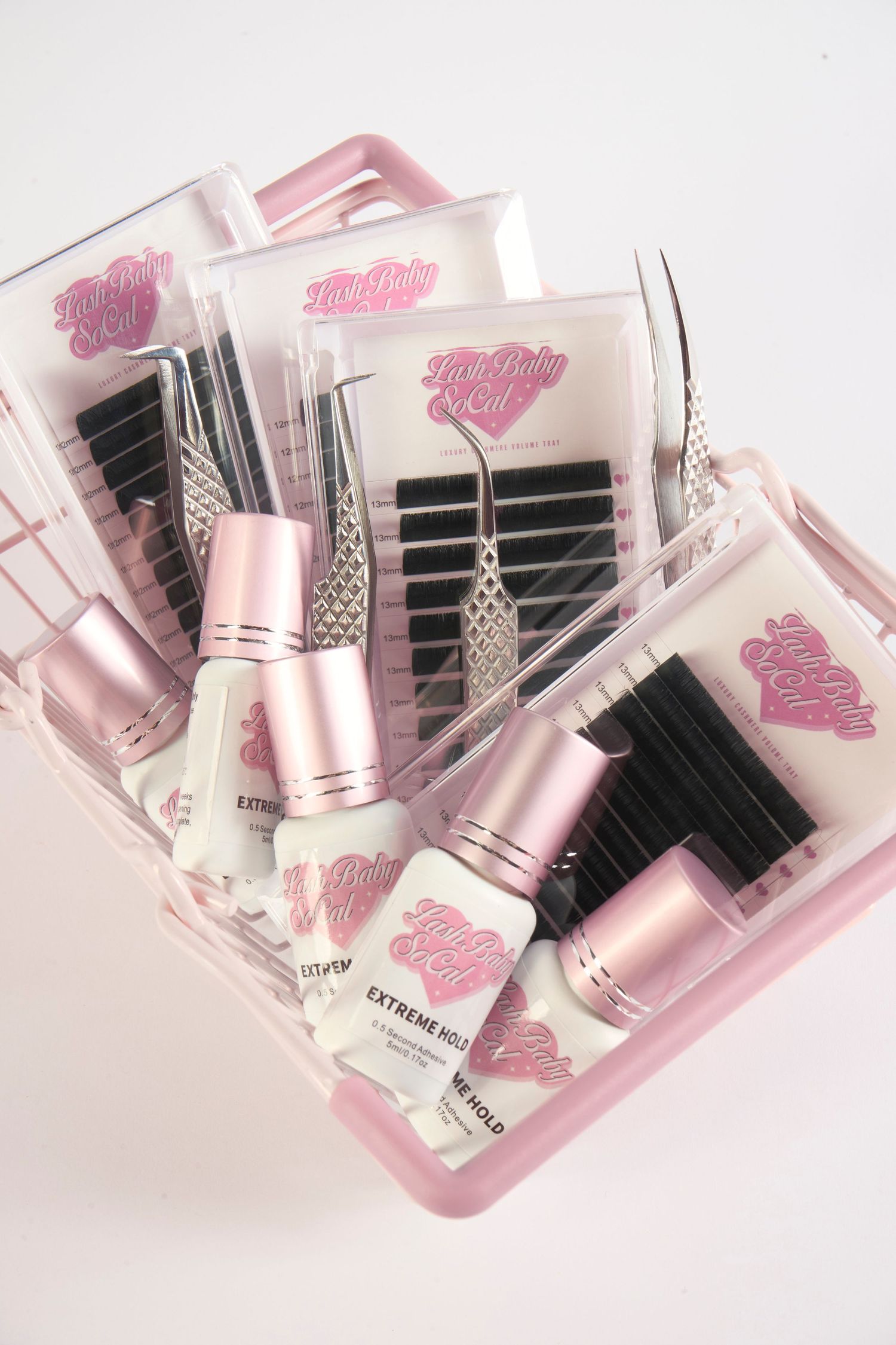 Pink lash extension kit with tweezers, glue, and lash trays in a pink organizer basket by Lash Baby SoCal.