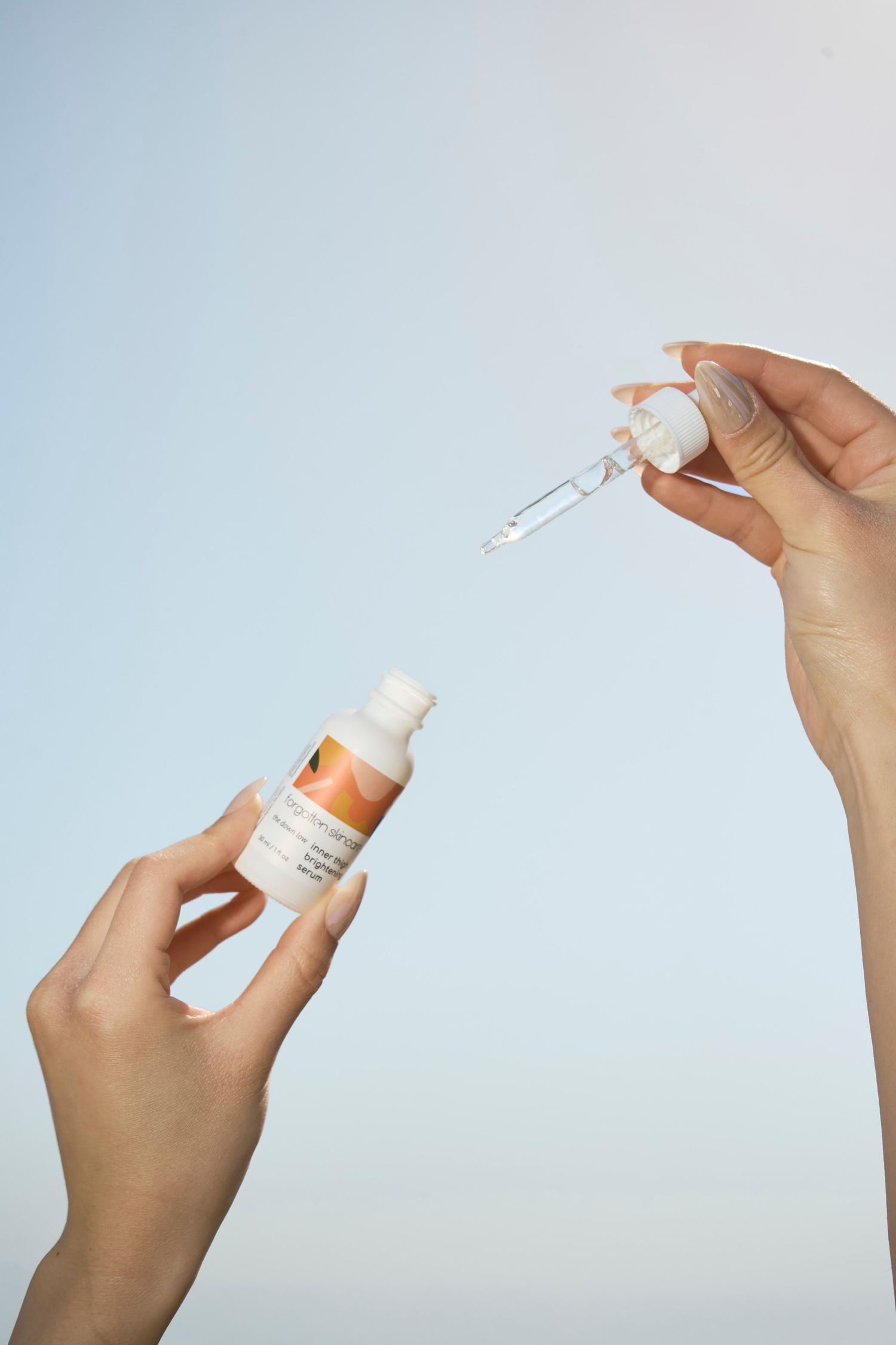 Hands holding a skincare serum bottle and dropper pipette against a light blue background.