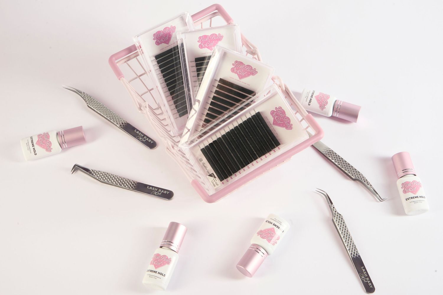 Pink eyelash extension kit with tweezers, lash trays, and adhesive bottles on white background.