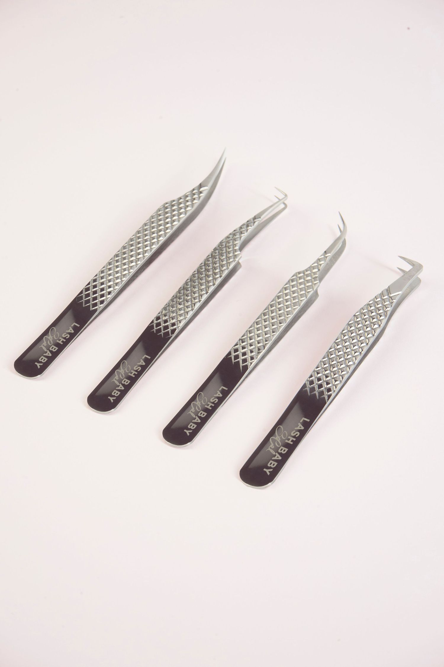 Four stainless steel tweezers with diamond-grip handles and varied tip styles arranged on a pink background.