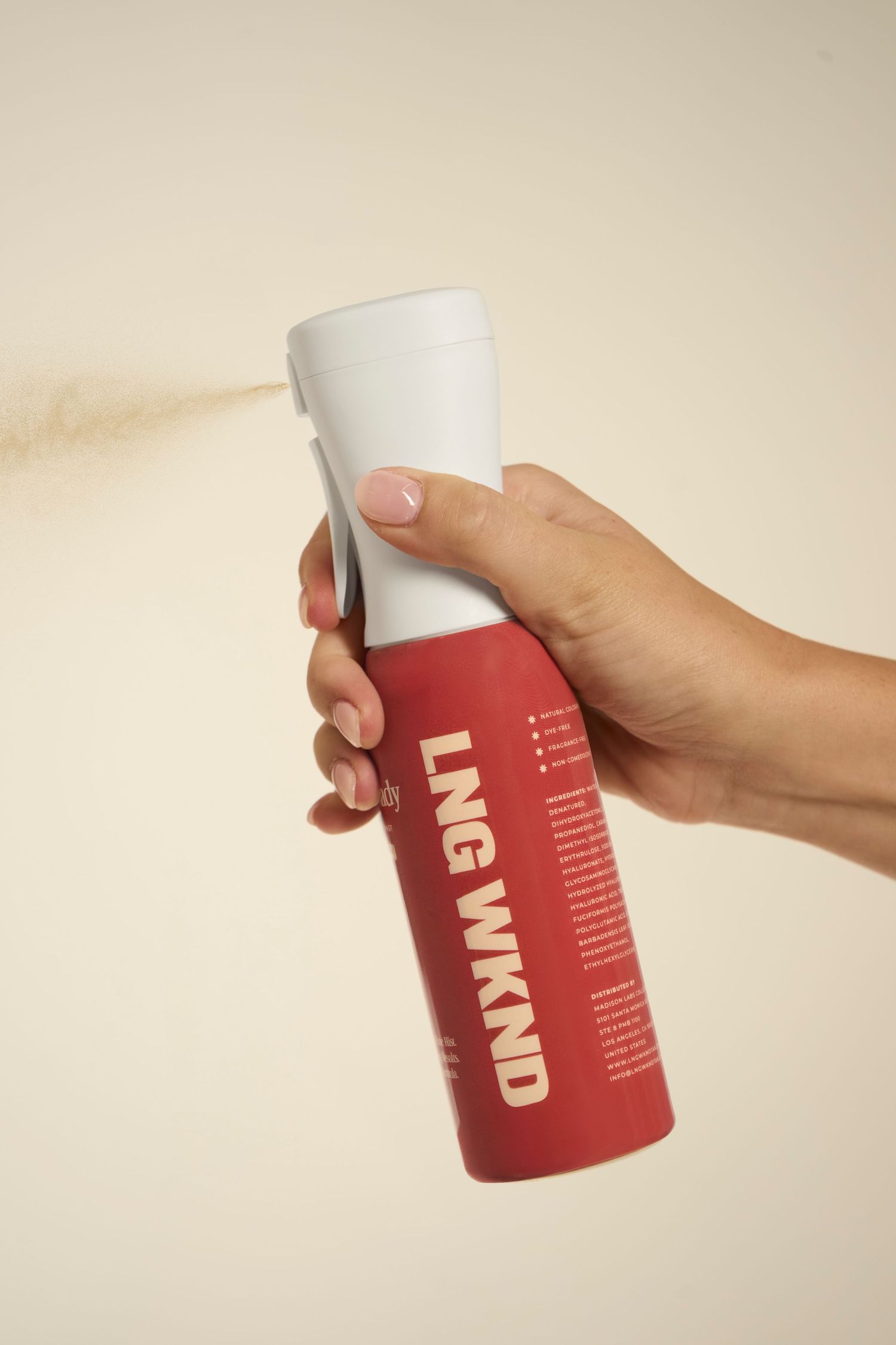 Hand spraying a red and white LNG WKND bottle against a neutral beige background.