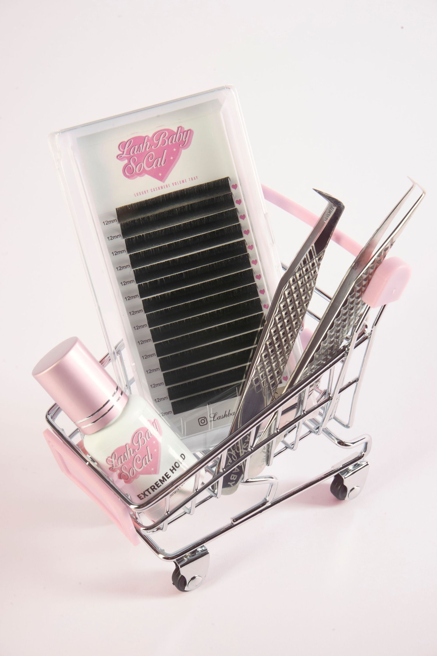 Pink mini shopping cart filled with lash extensions tray, tweezers, and adhesive bottle from Lash Baby SoCal.