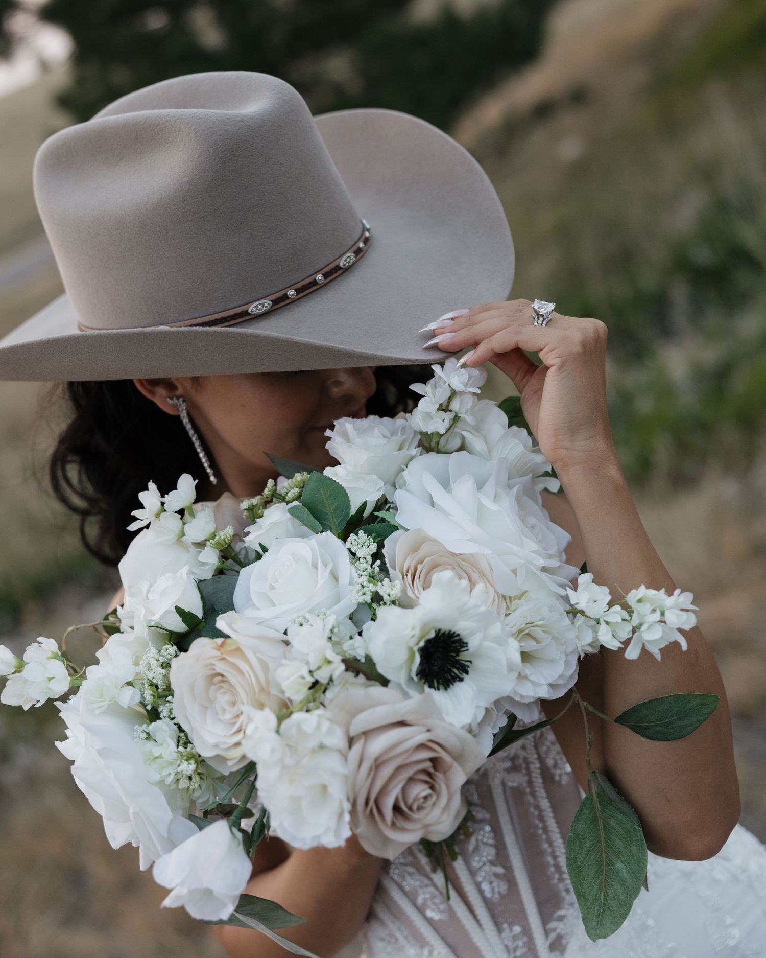 Bride in white dress and tan cowboy hat holding a white and blush floral bouquet.
